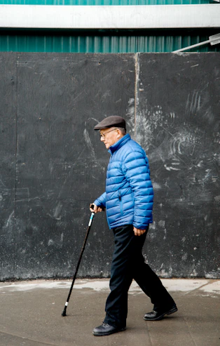 Un homme âgé en veste bleue marche avec une canne.