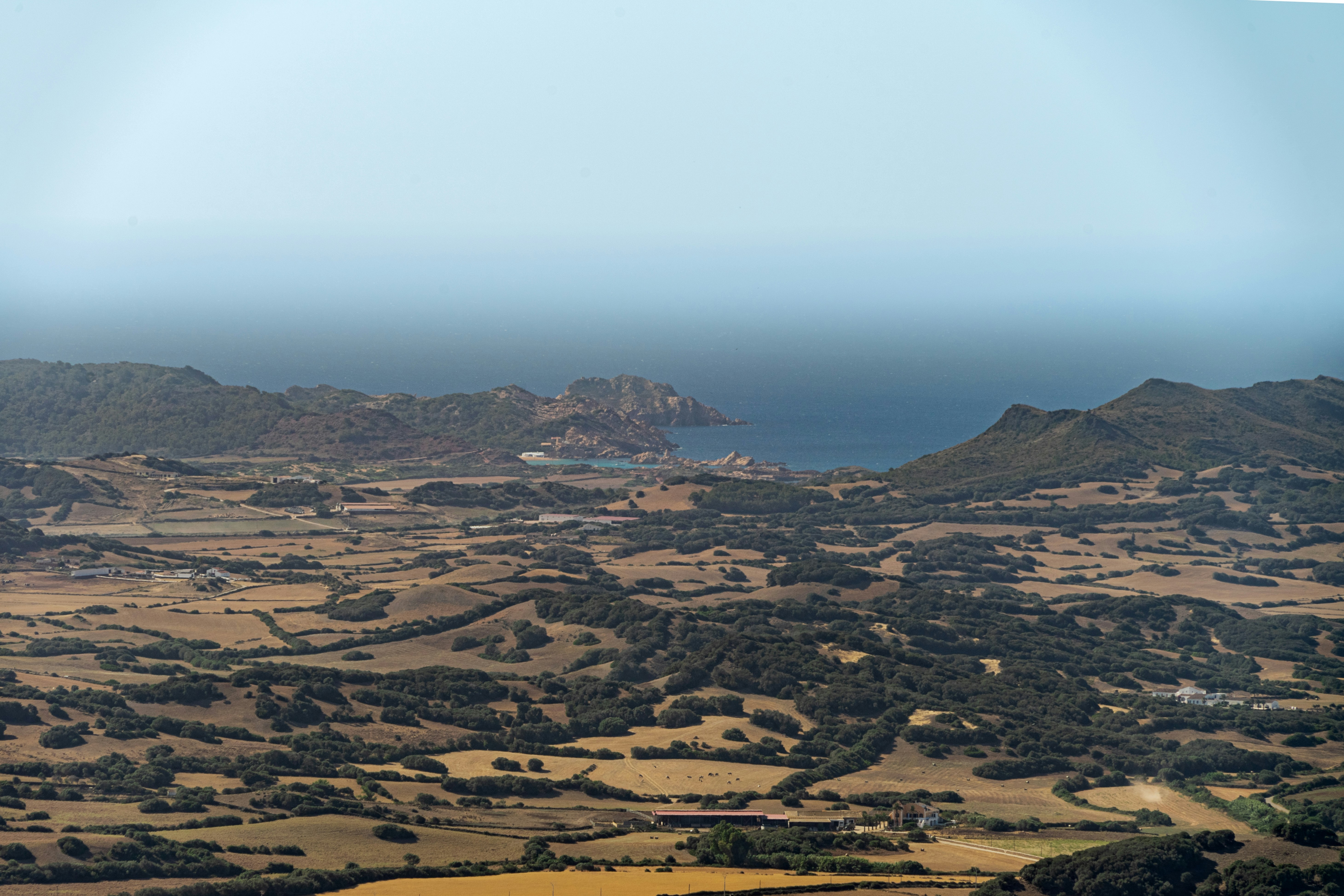 Expansive rural landscape with distant sea and hills.