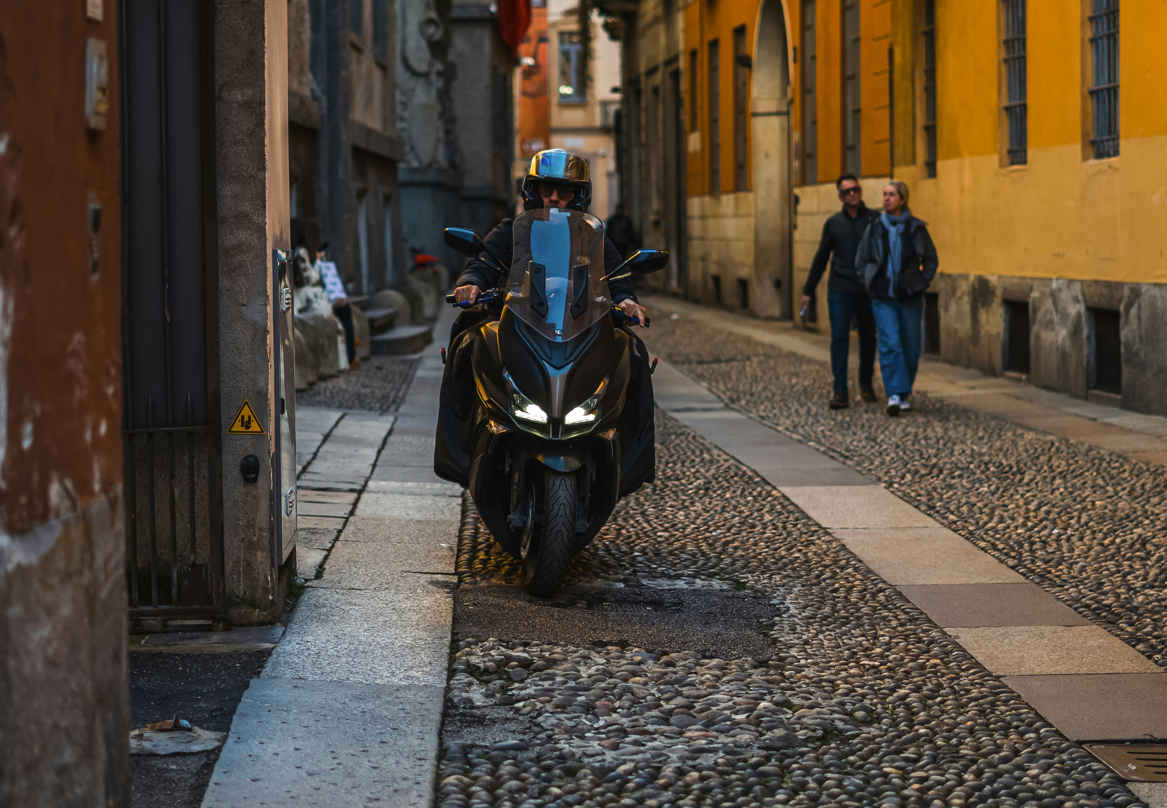 Man riding a motorcycle down a narrow cobblestone street.