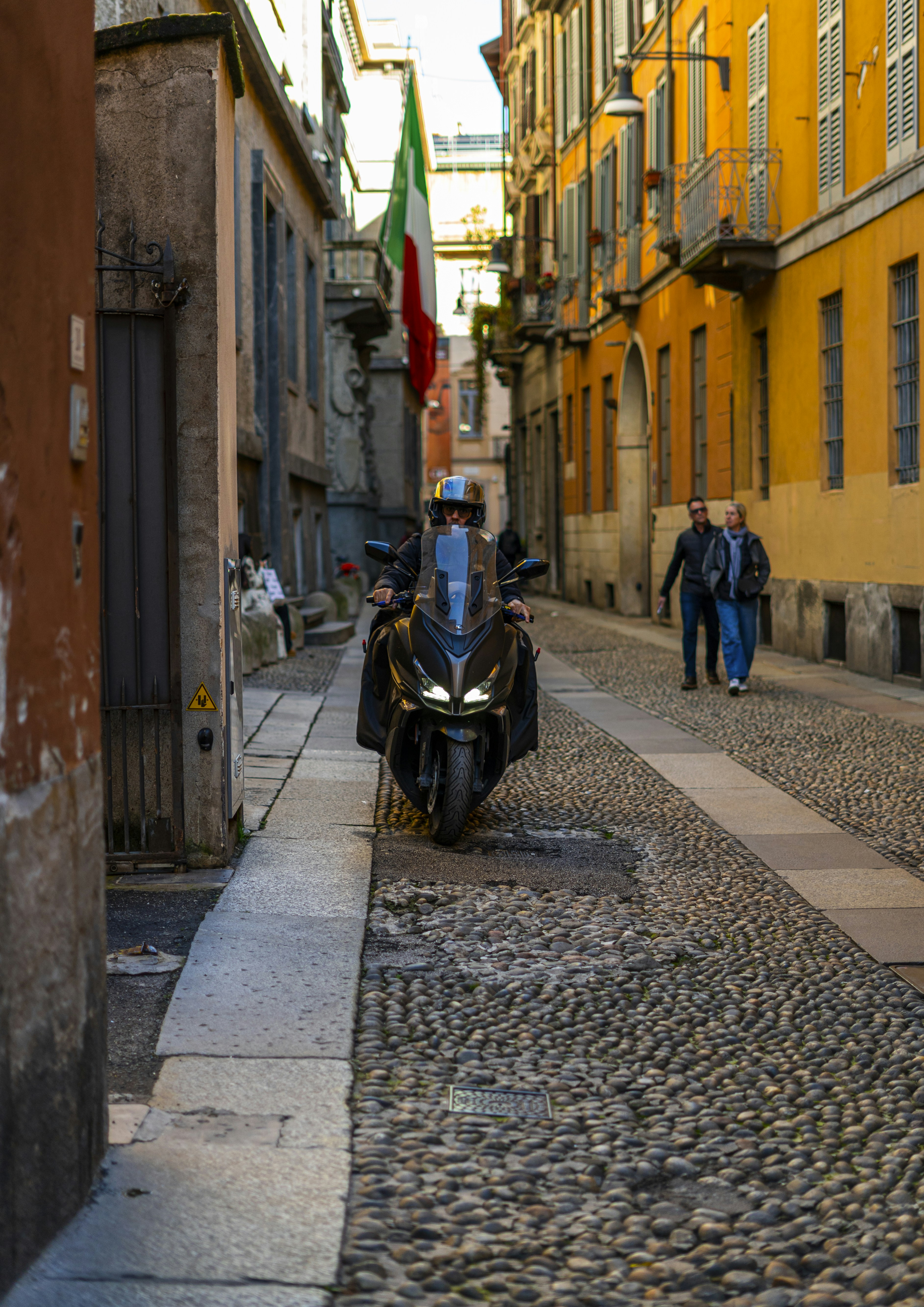 Man riding a scooter down a cobblestone street.