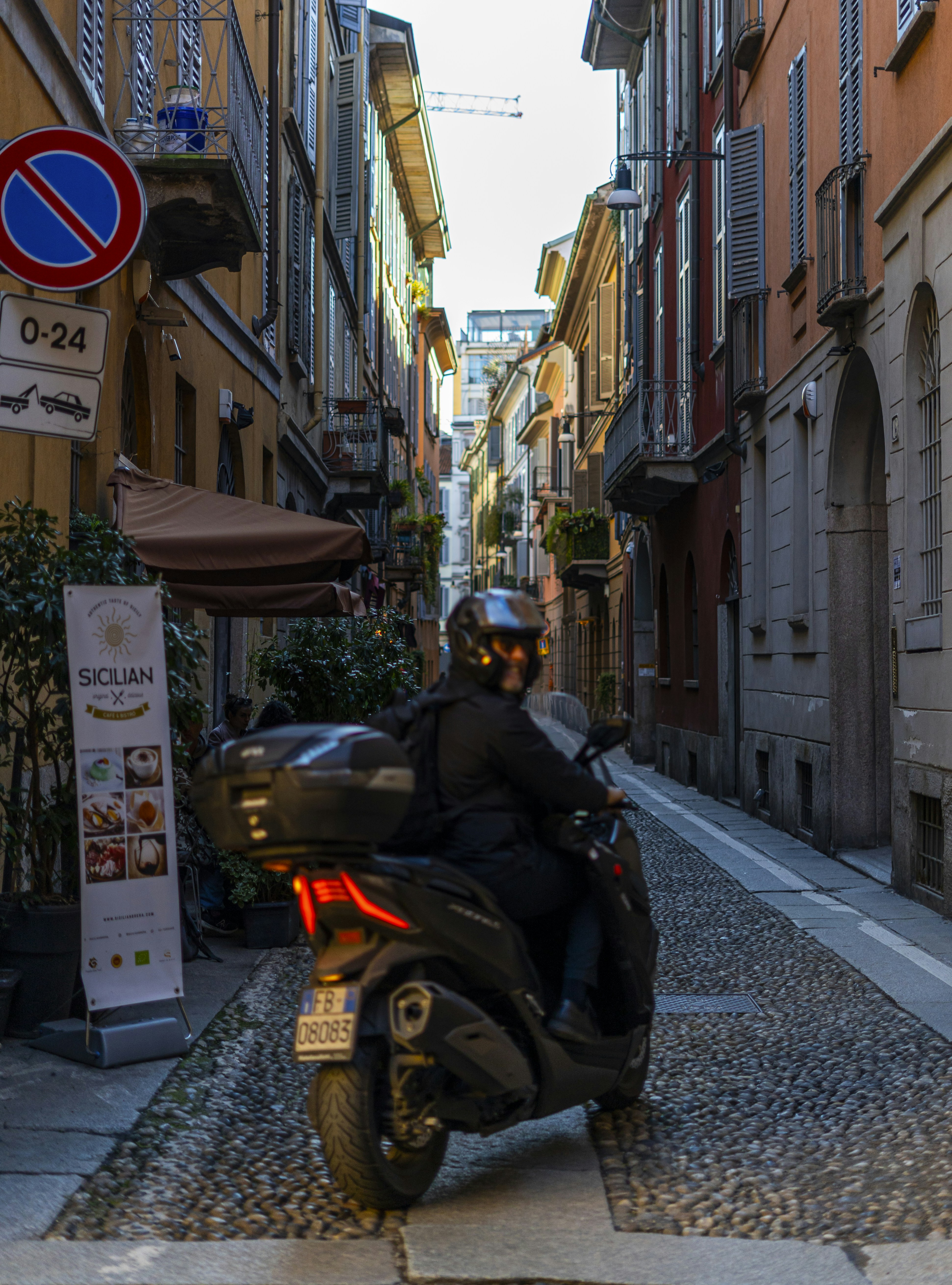 Person riding a scooter down a narrow cobblestone street.