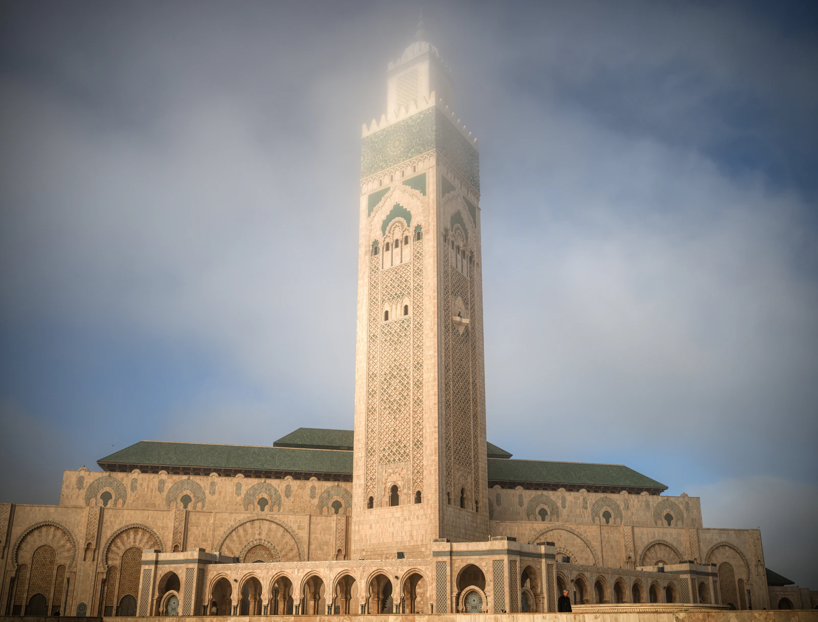 Tall carved minaret of a grand mosque rising through soft morning mist