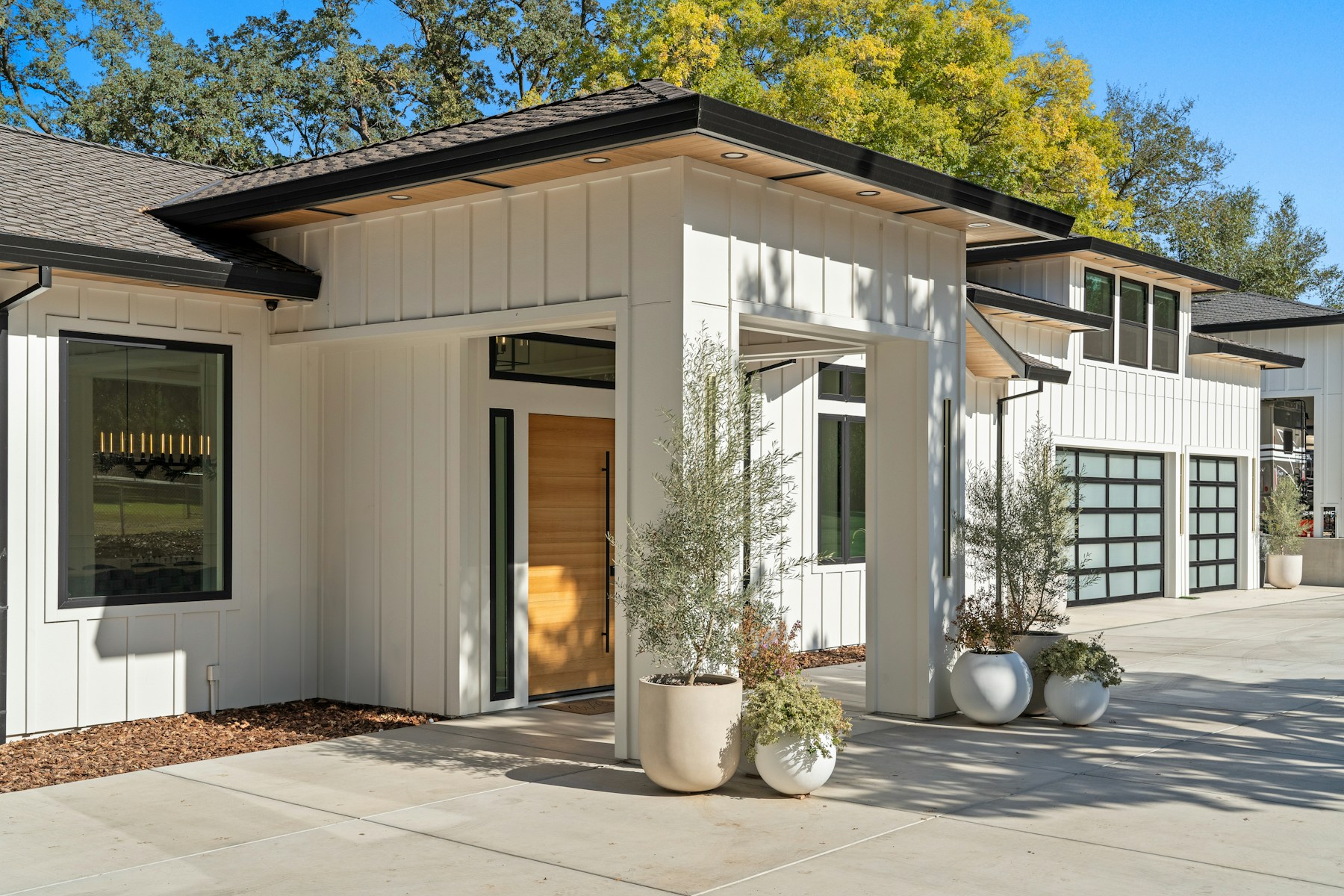Modern white house with glass garage doors and plants under bright blue sky