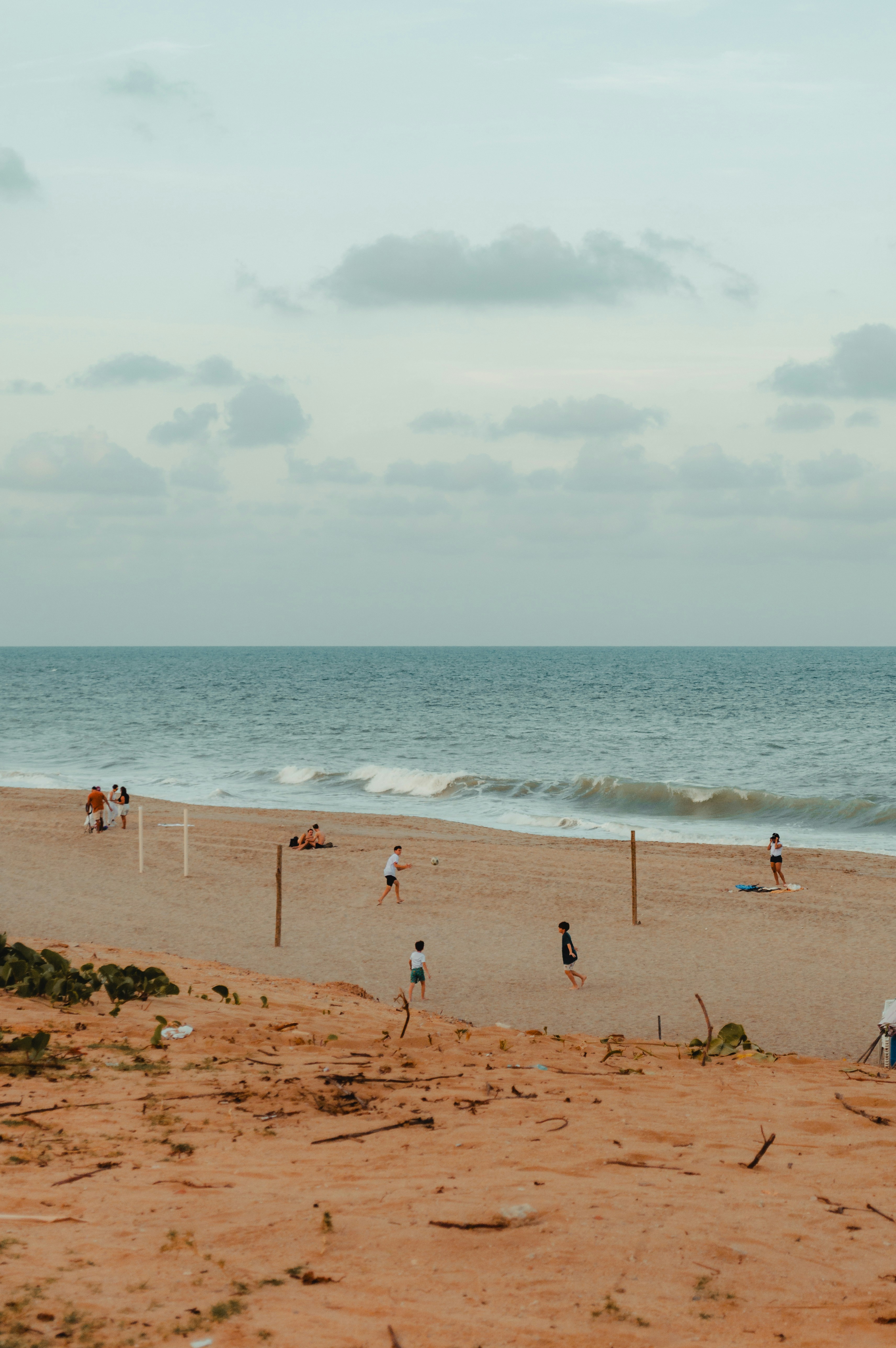 People play volleyball on a sandy beach by the ocean.