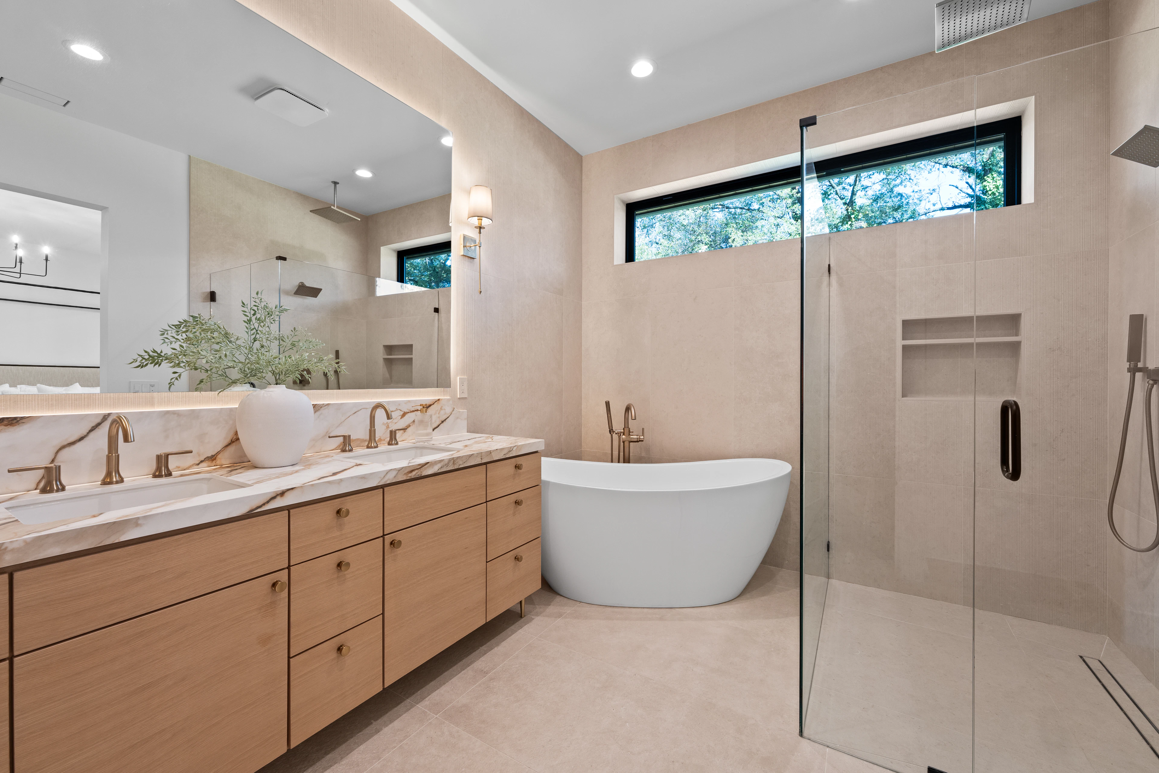 Oak double vanity, pale stone surfaces, freestanding bathtub and glass shower enclosure.