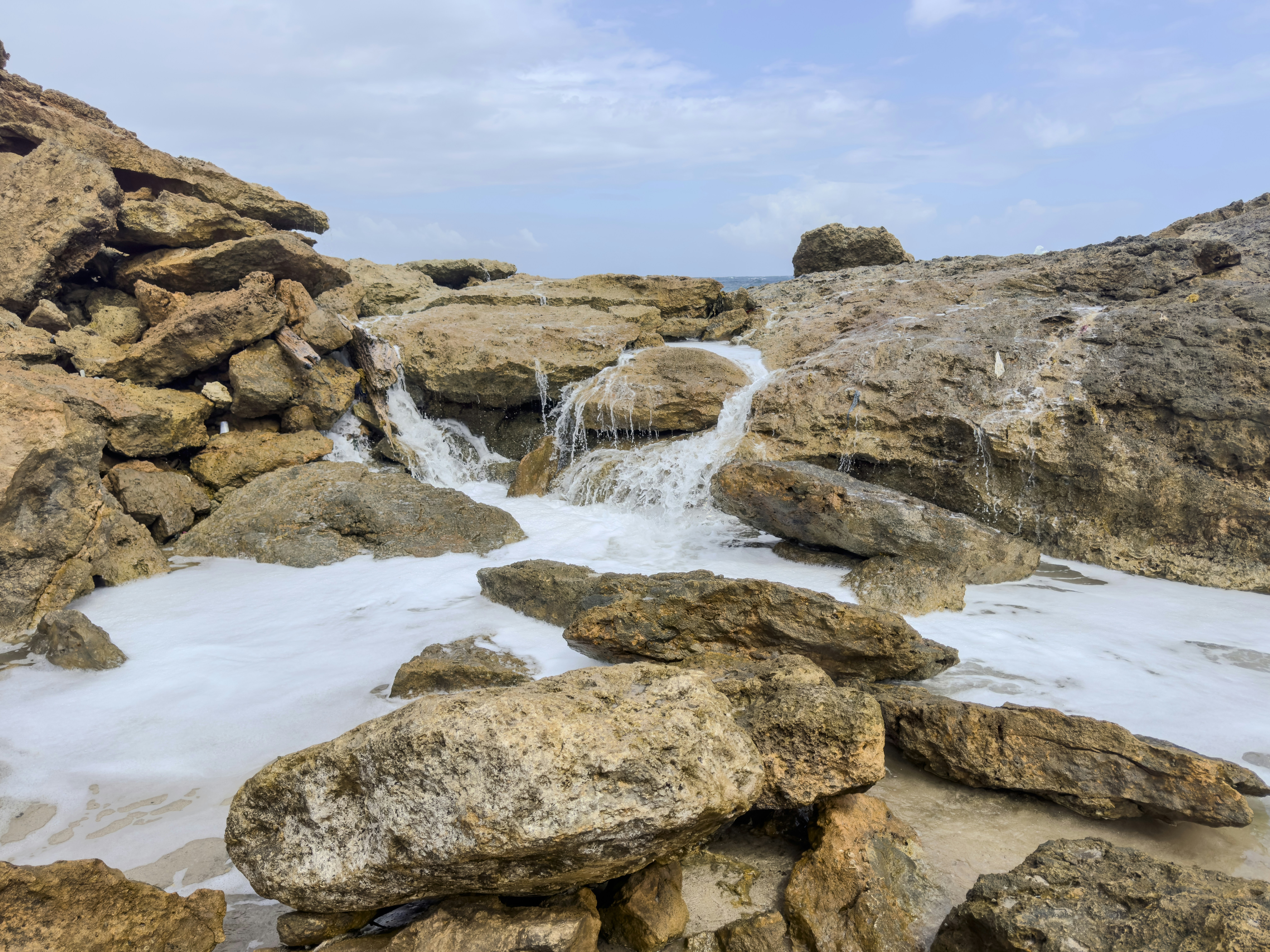 Wasser stürzt über Felsen in ein schaumiges Meer.