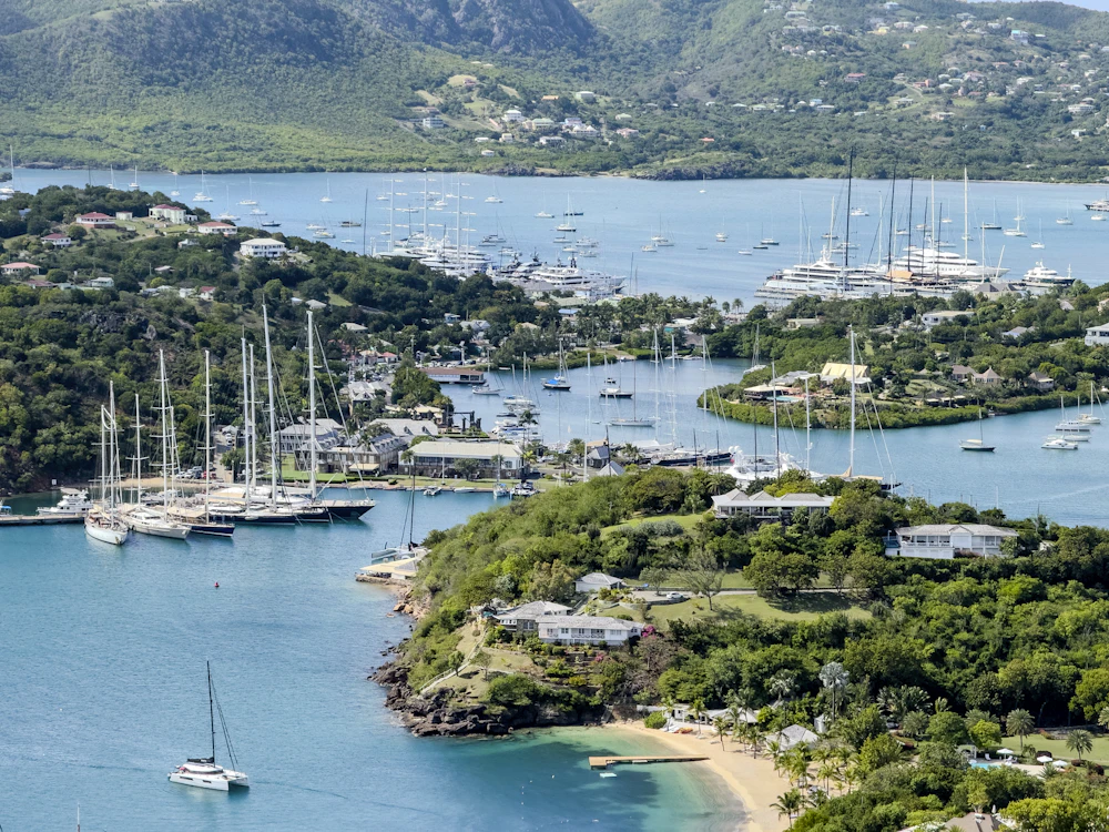 Mehrere Segelyachten ankern in einer türkisen Karibikbucht vor grünen Hügeln