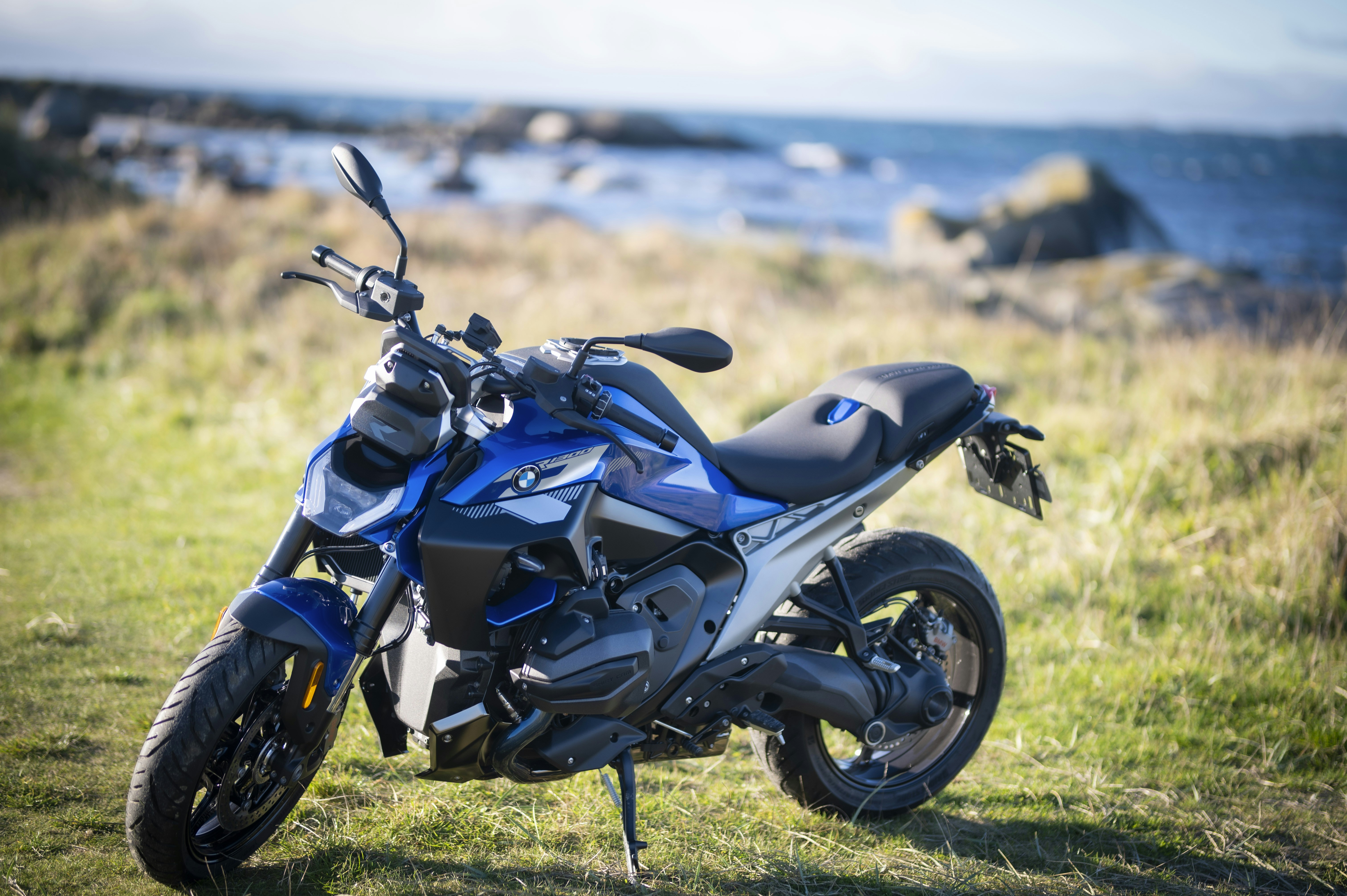 A blue motorcycle parked on grassy terrain by the sea.