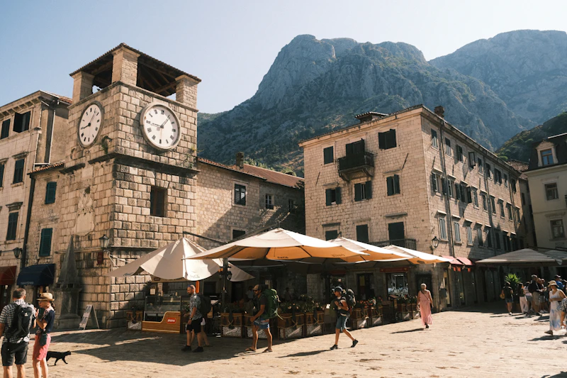 The leaning clock tower on Arms Square in Kotor's Old Town, with cafés and the mountains behind