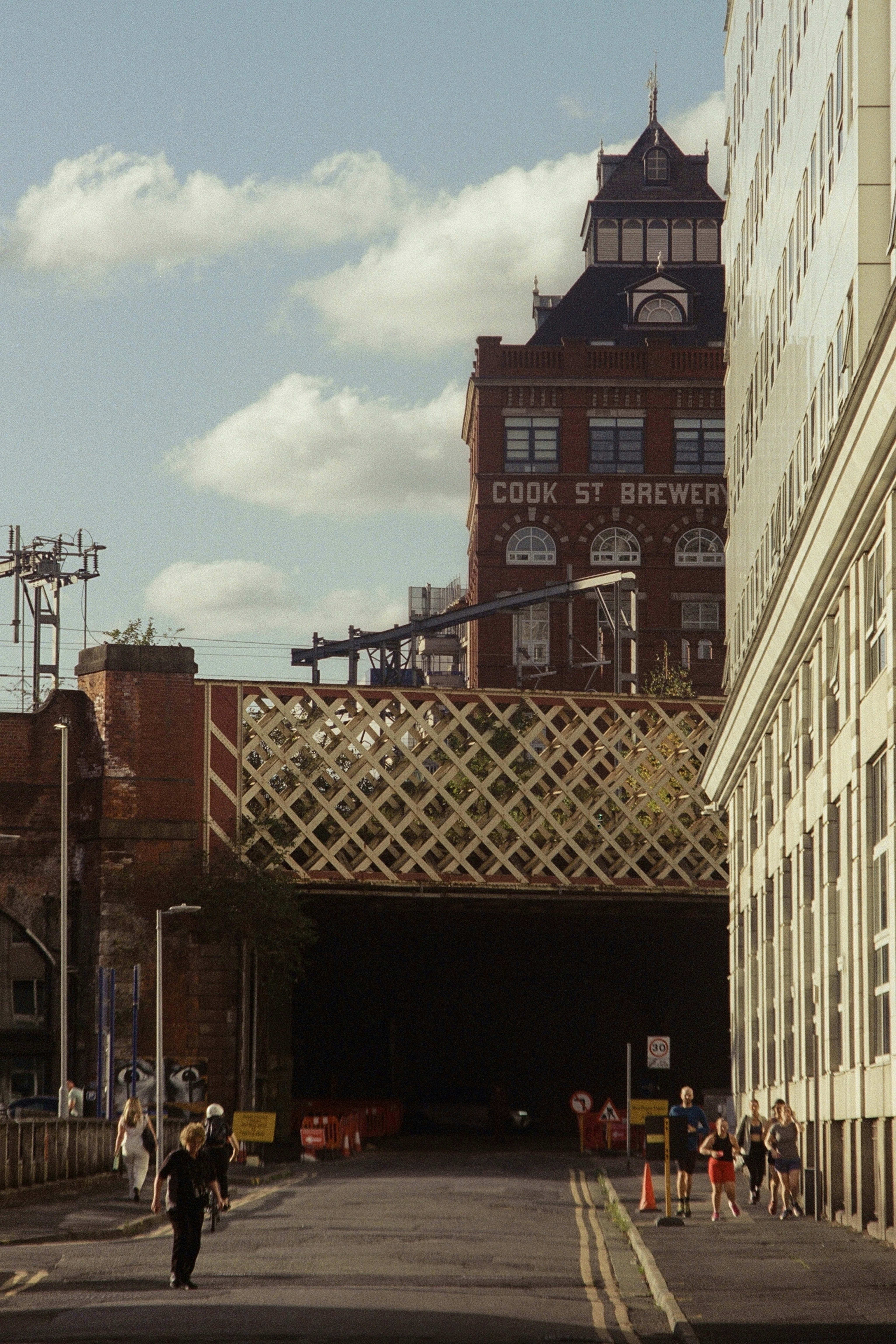 People walk down a street under a bridge near buildings
