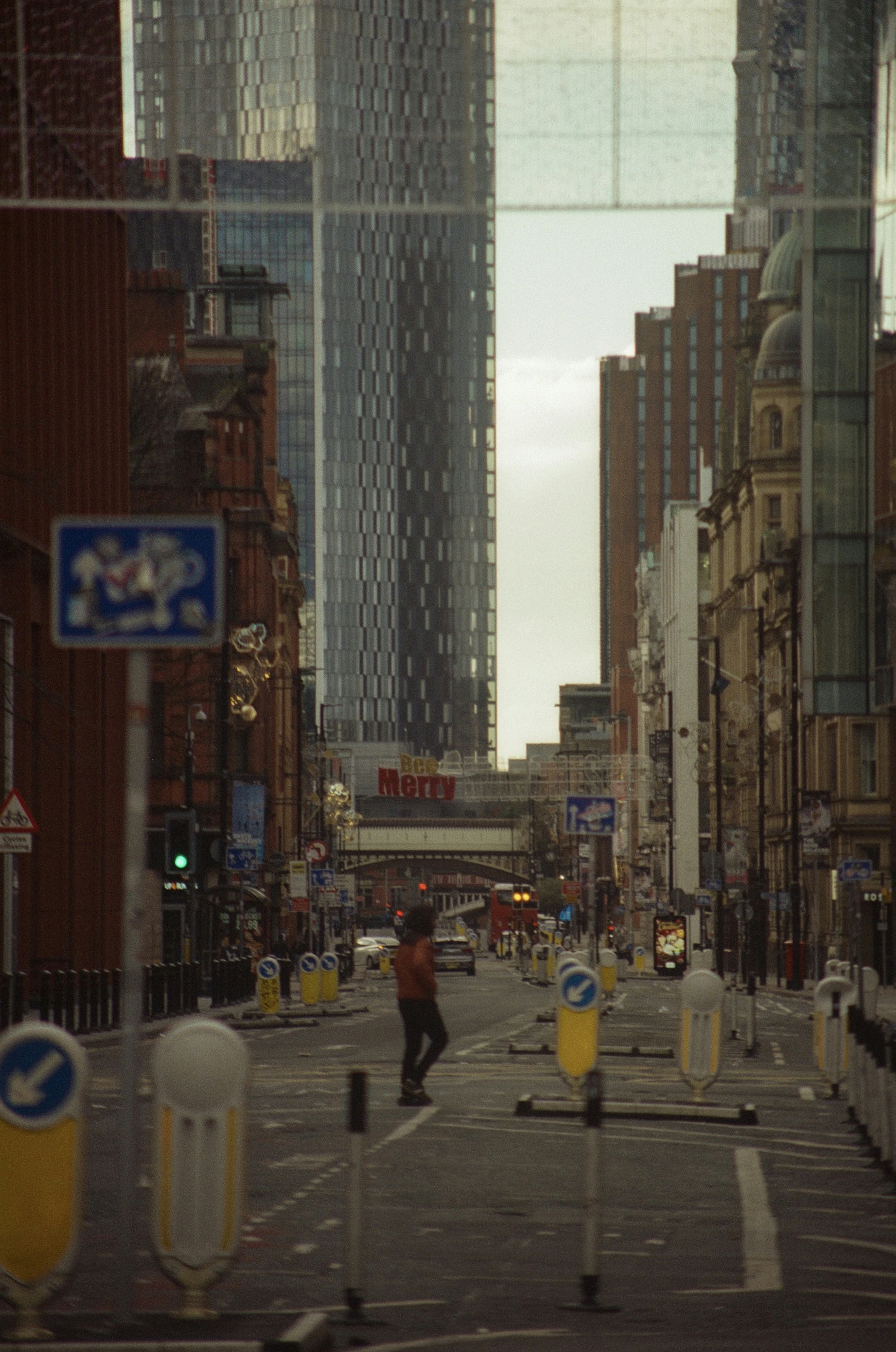 A person crosses a city street with tall buildings.