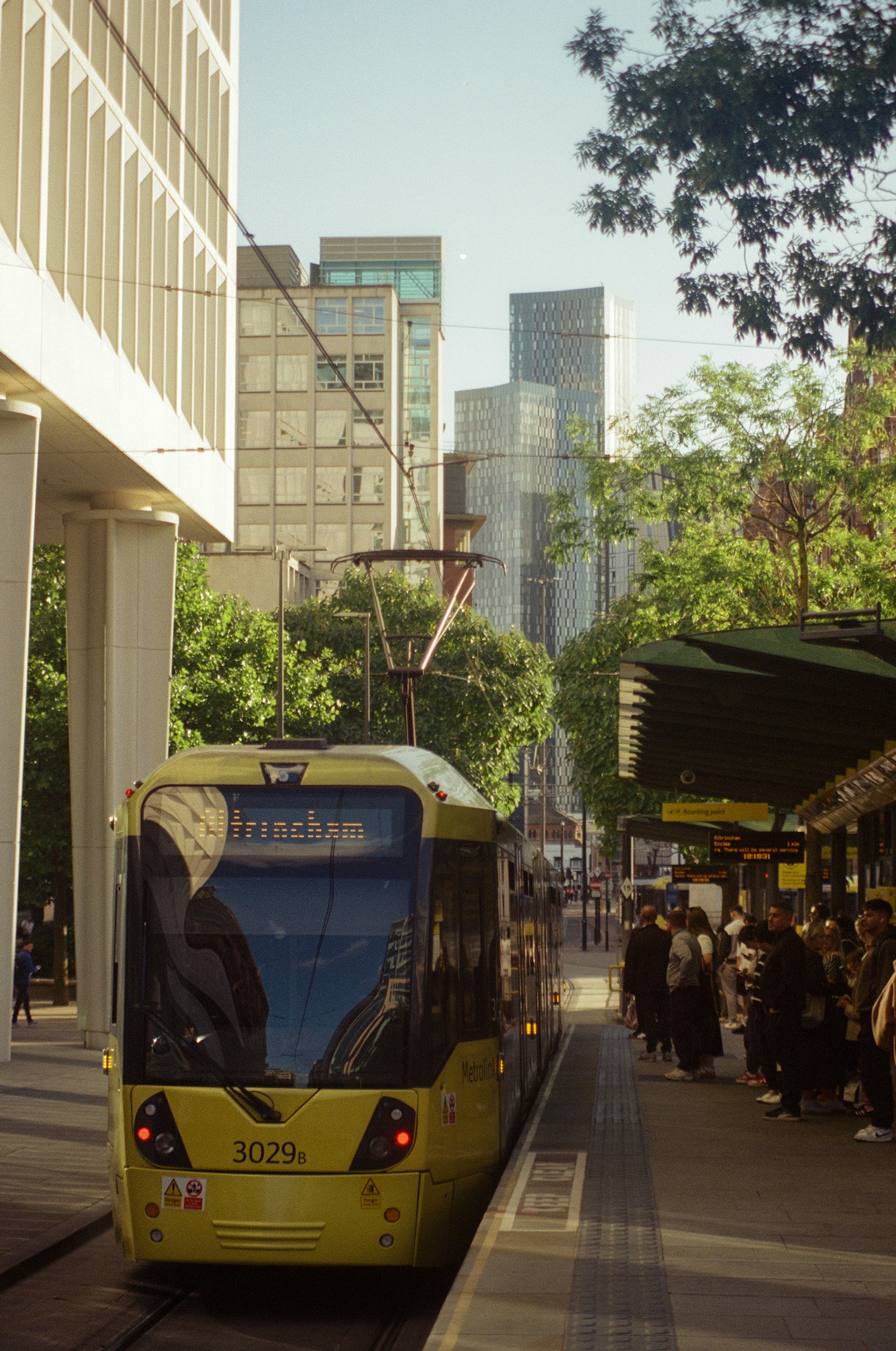 Yellow tram at station with modern buildings behind.