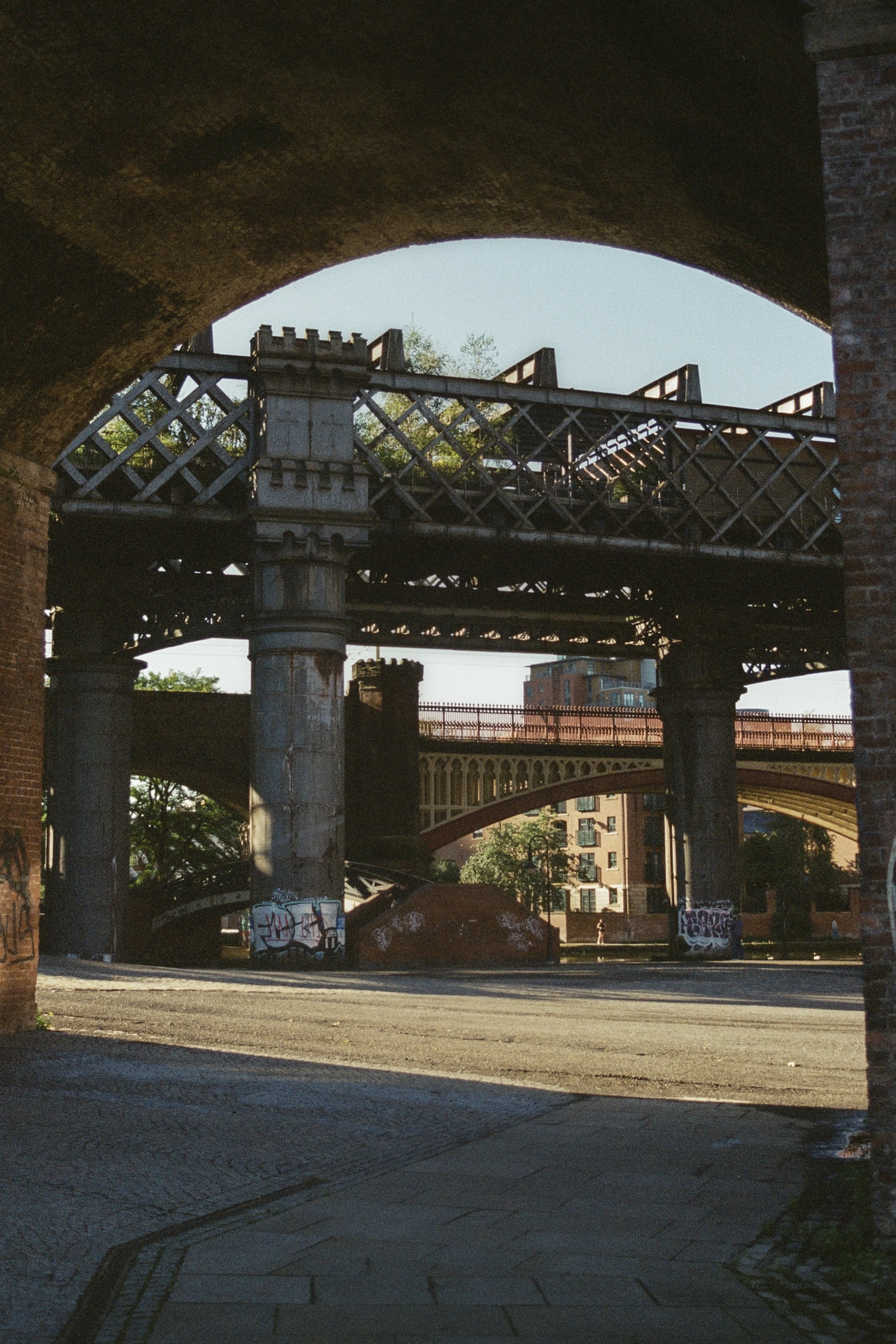 The stacked cast-iron railway viaducts of Castlefield in Manchester, their latticed girders and castellated stone piers framed through a dark brick arch.