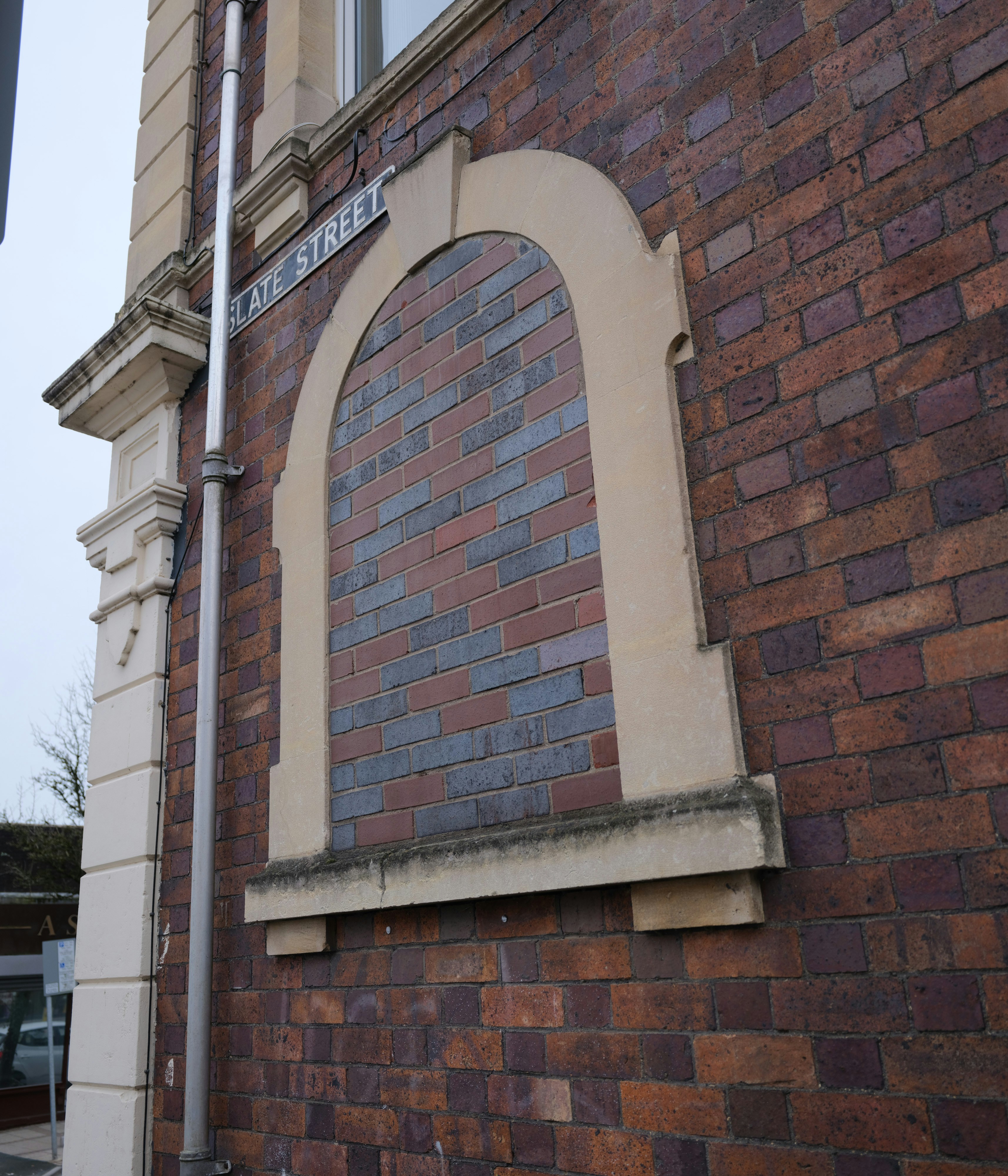 Backsteinwand mit gewölbtem, vernageltem Fenster.