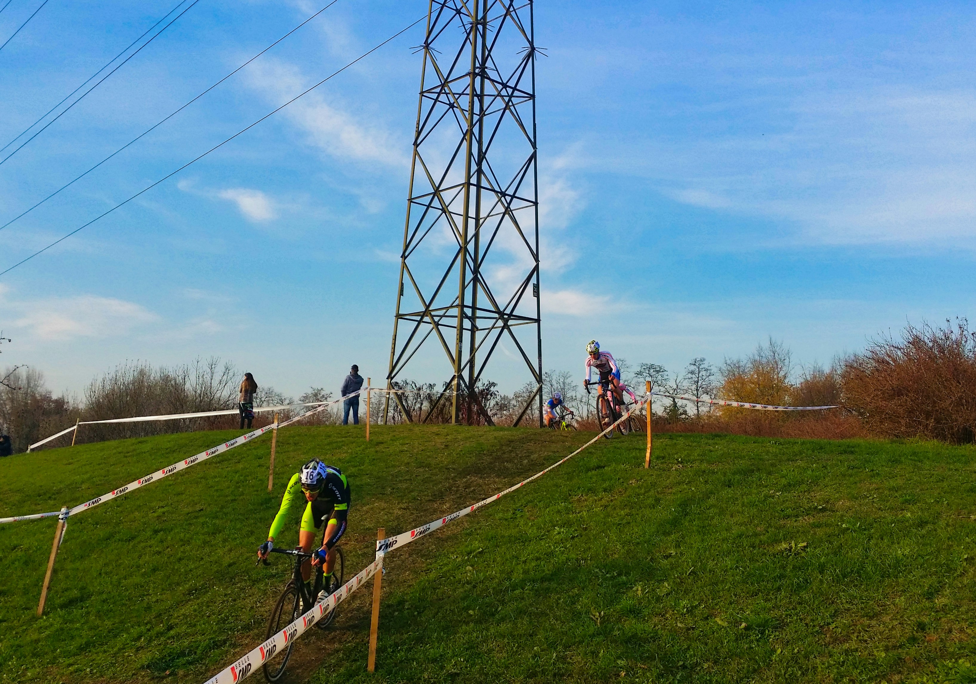 Cyclists race up a grassy hill under a pylon