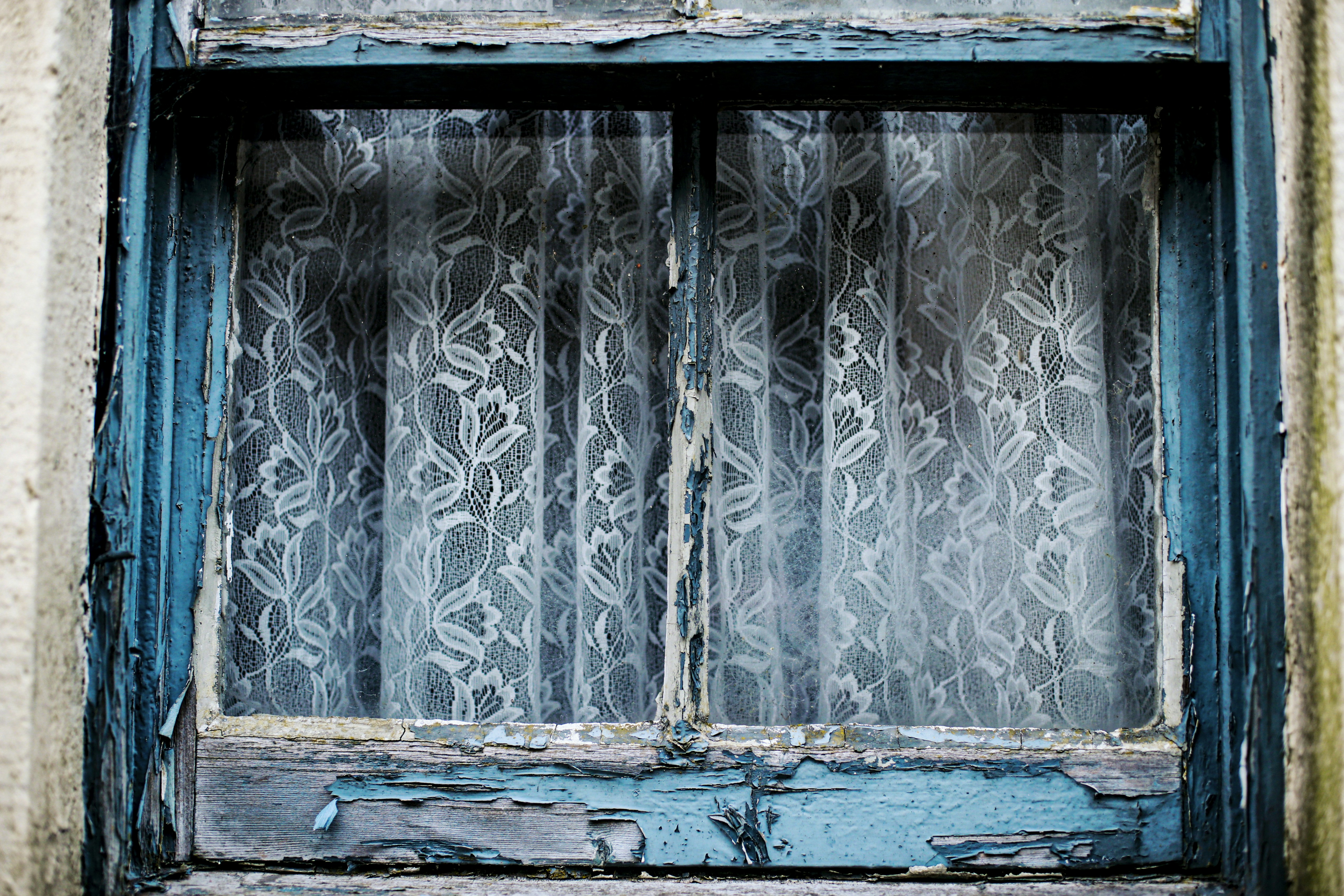 Altes verwittertes Fenster mit weißen Spitzenvorhängen