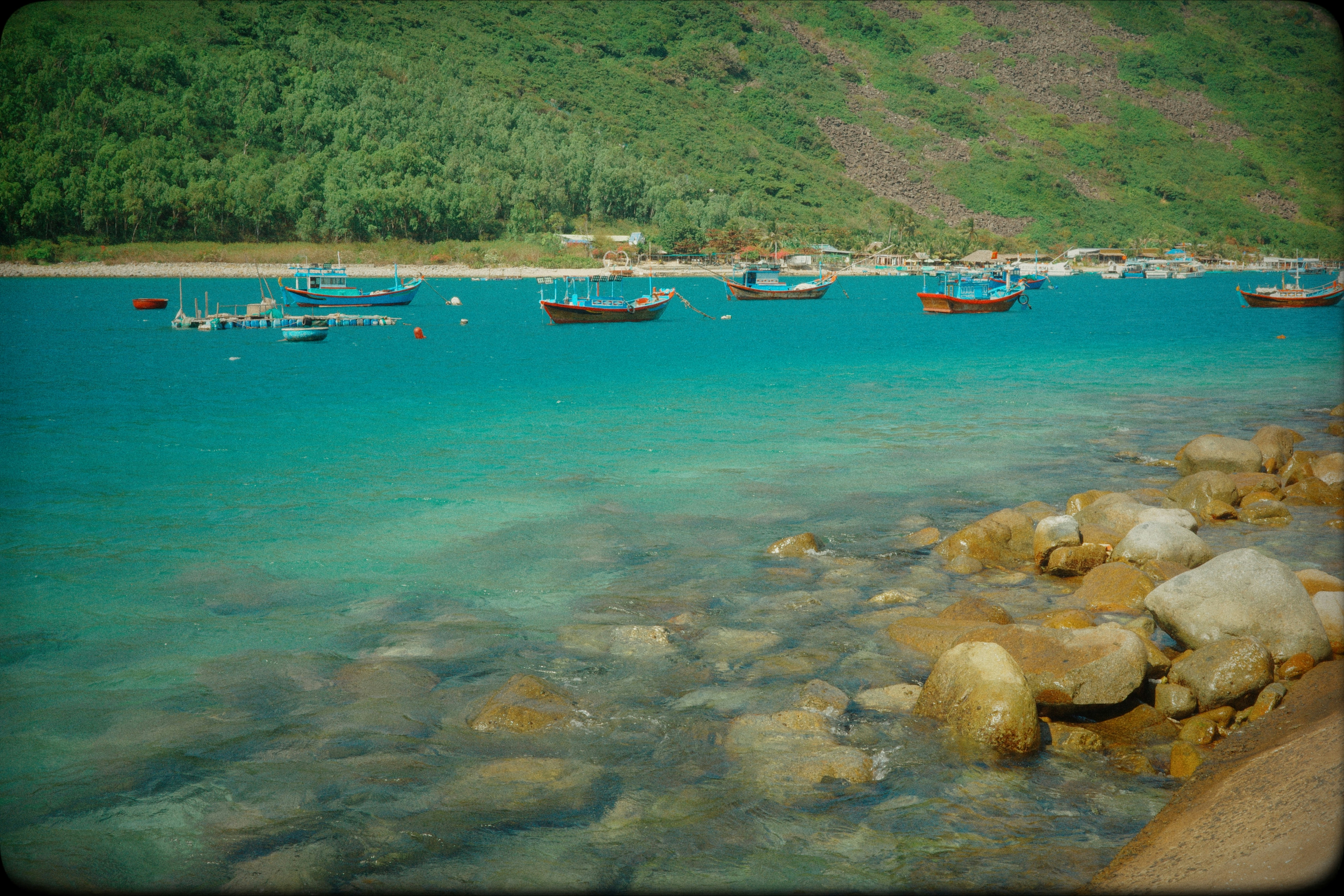 Boats float on clear turquoise water near a rocky shore