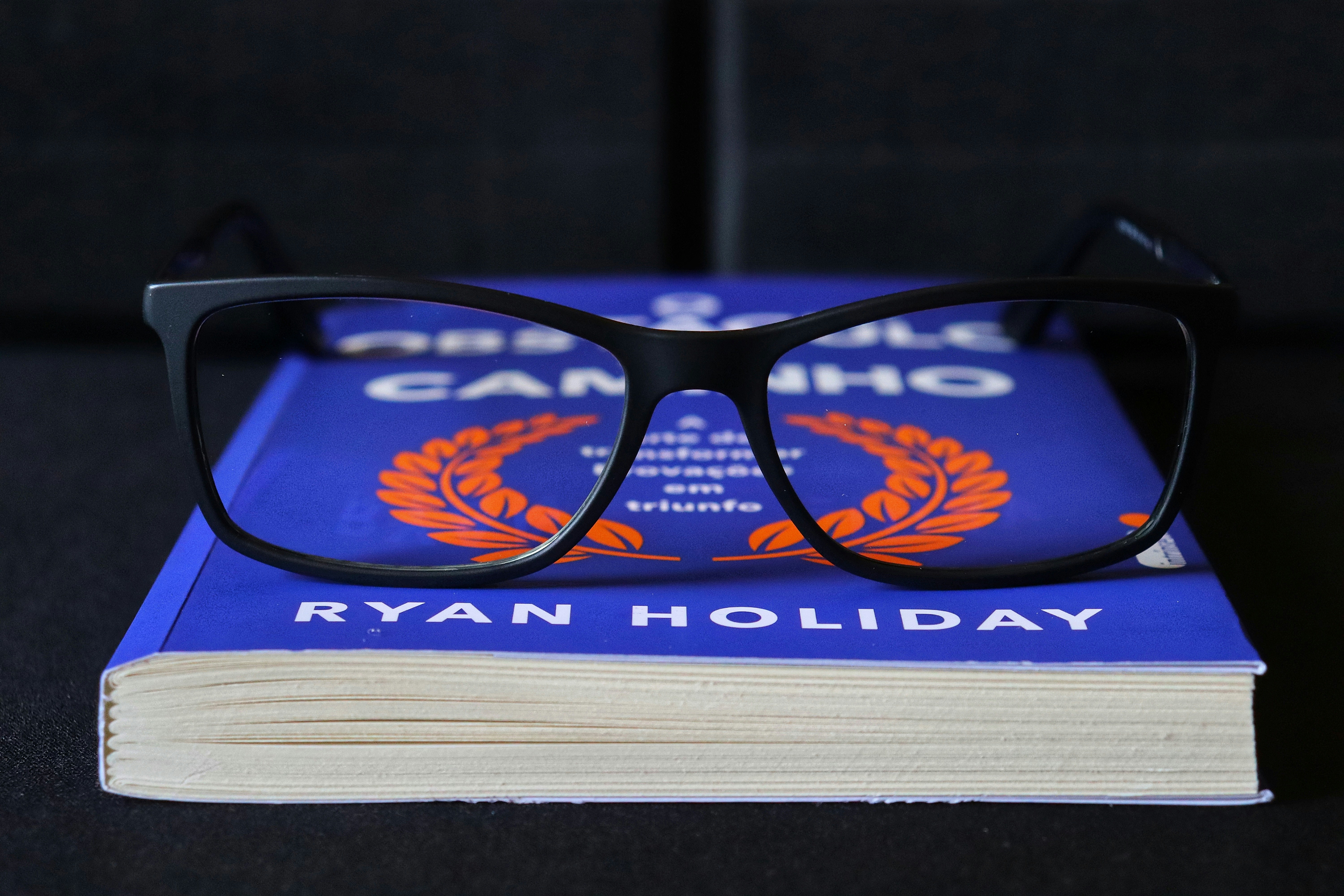 Des lunettes posées sur un livre bleu de Ryan Holiday.