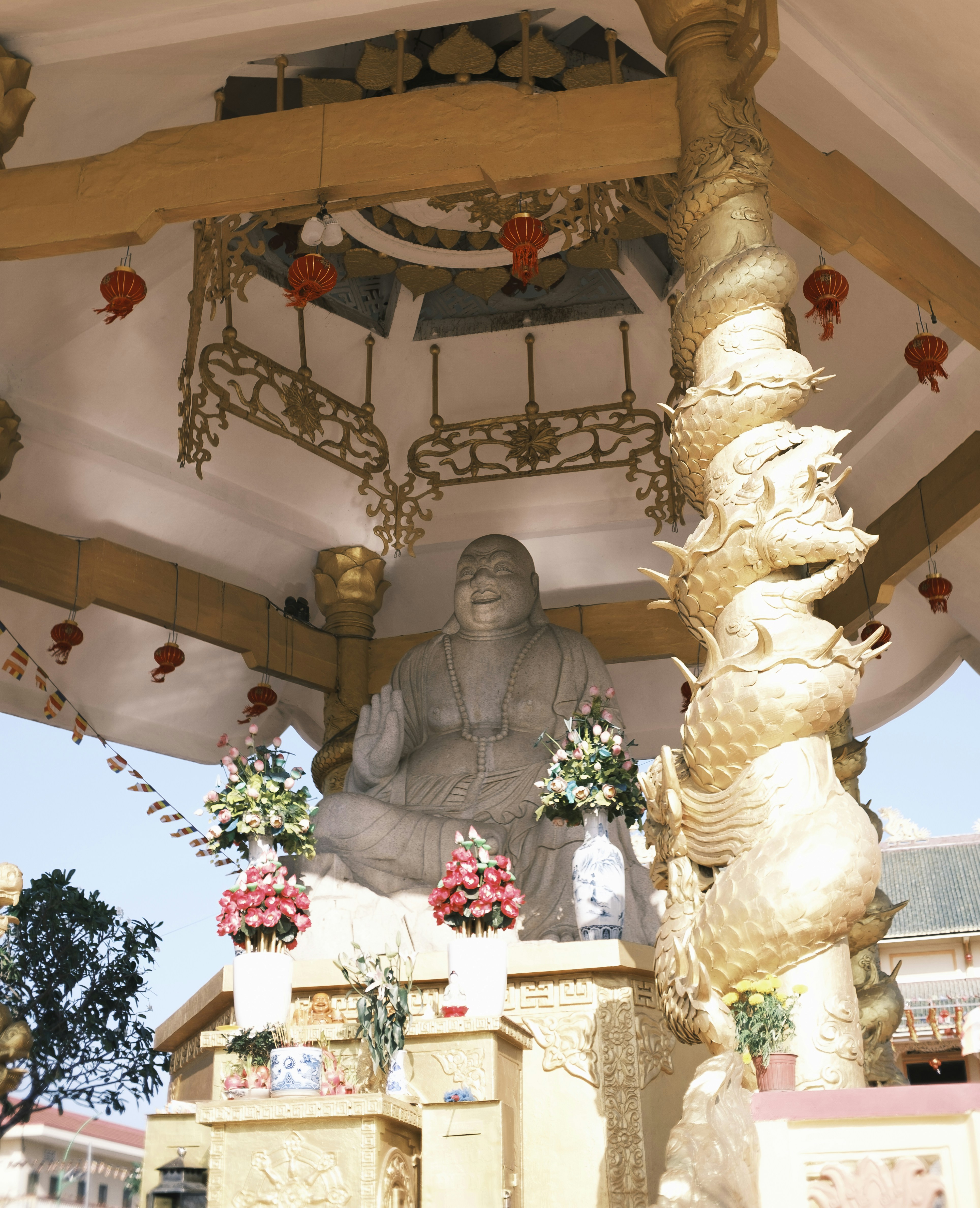 A large buddha statue sits within a golden dragon-adorned pavilion.
