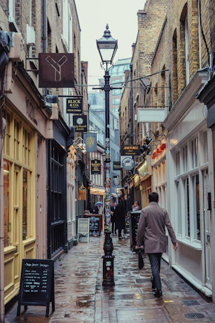 A man walks down a narrow, wet london street