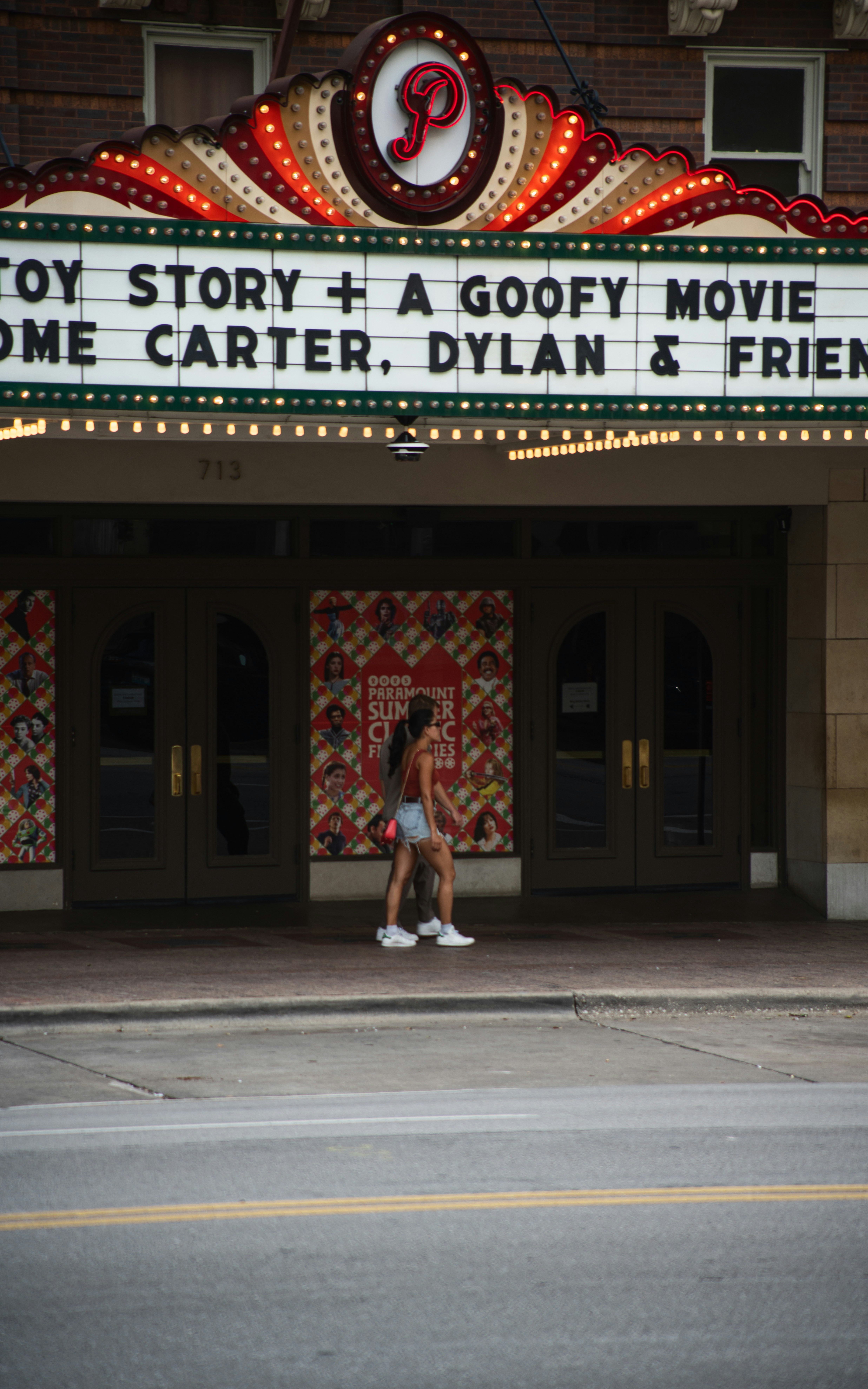 A woman walks past a marquee theater with movie titles.