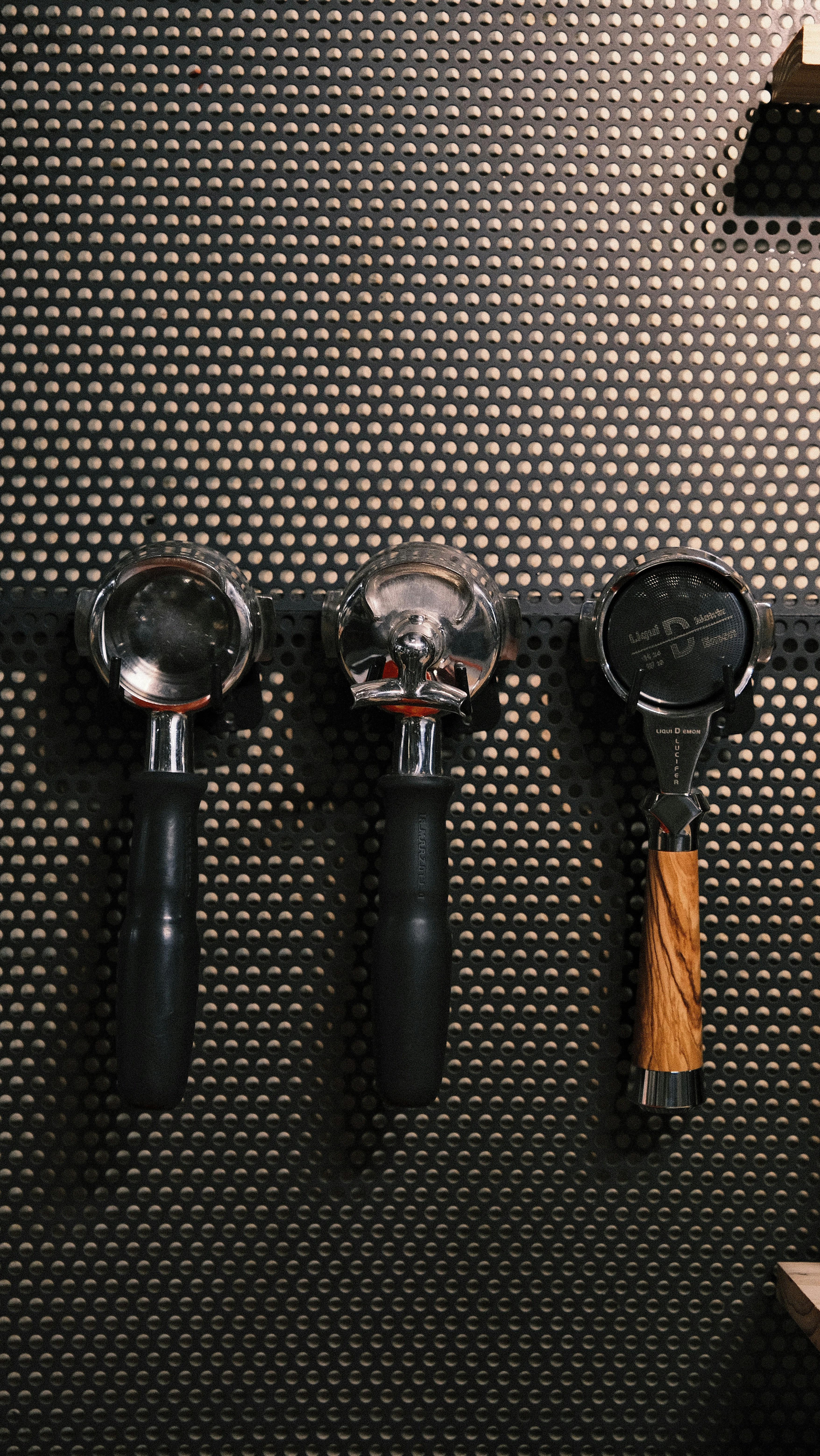 Three espresso portafilters hanging on a perforated wall