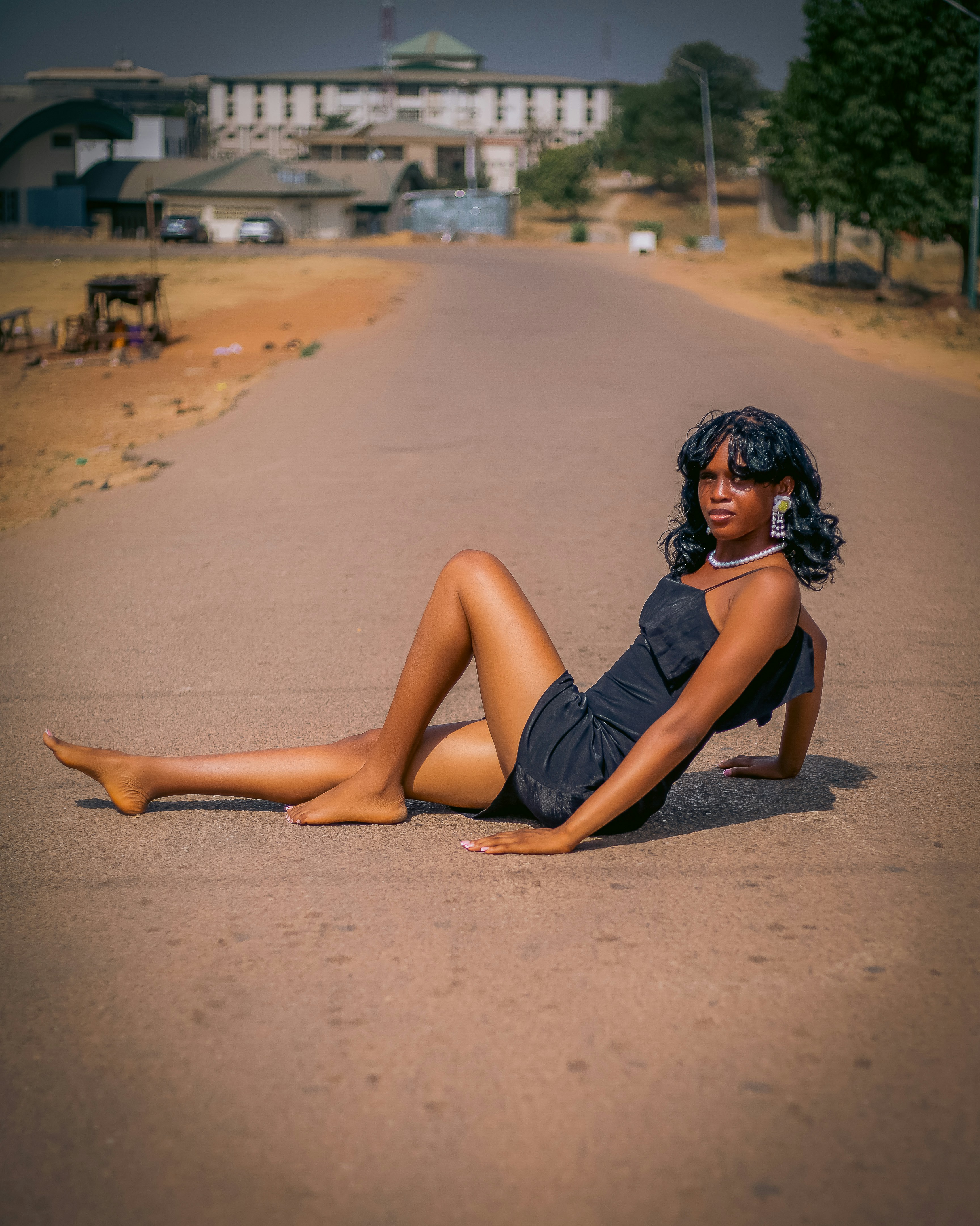 Giovane donna in abito nero sdraiata su una strada asfaltata