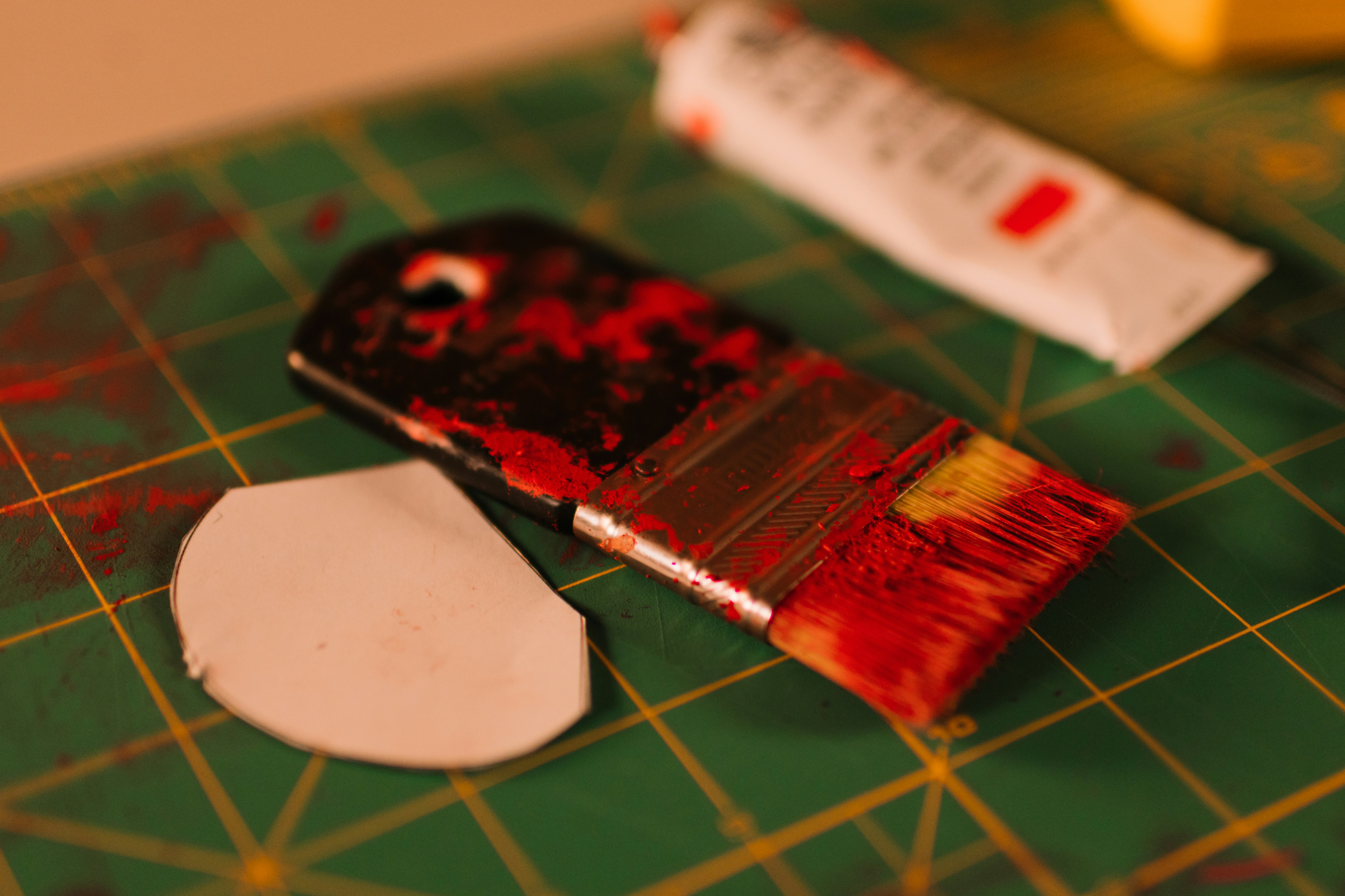 Paintbrush with red paint and tube on cutting mat
