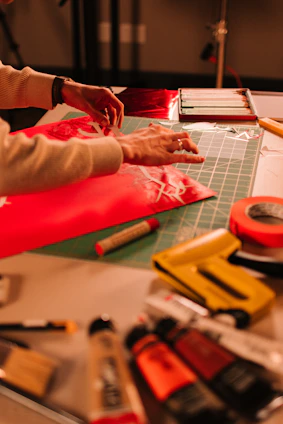 Hands working on a red material with craft supplies.