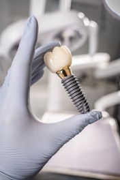 Gloved hand holding a dental implant and crown.