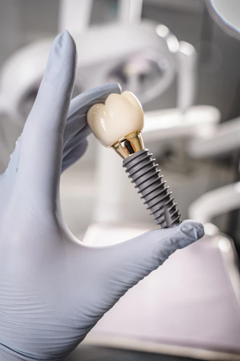Gloved hand holding a dental implant and crown.
