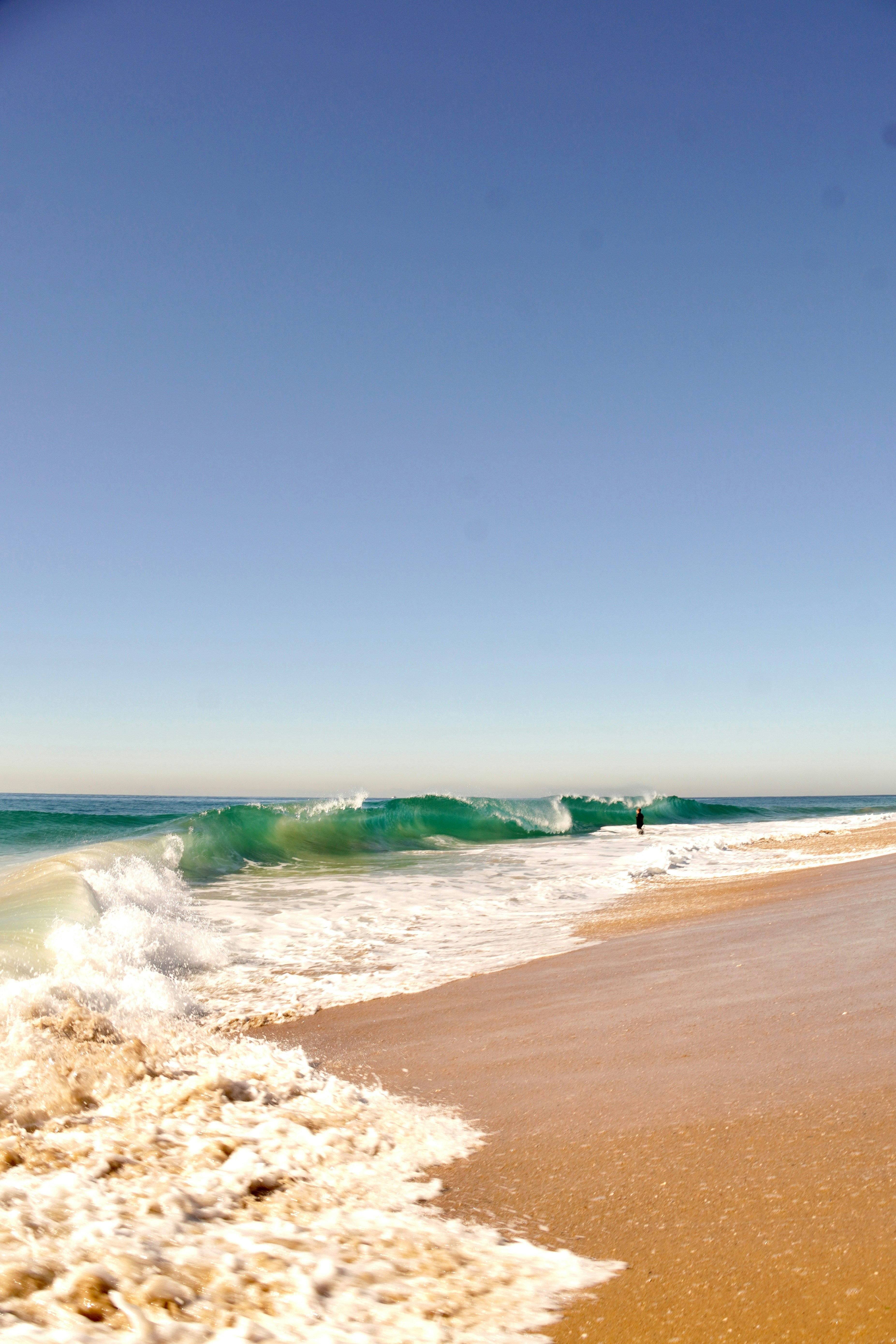 Turquoise wave crashes on a sandy beach under clear sky