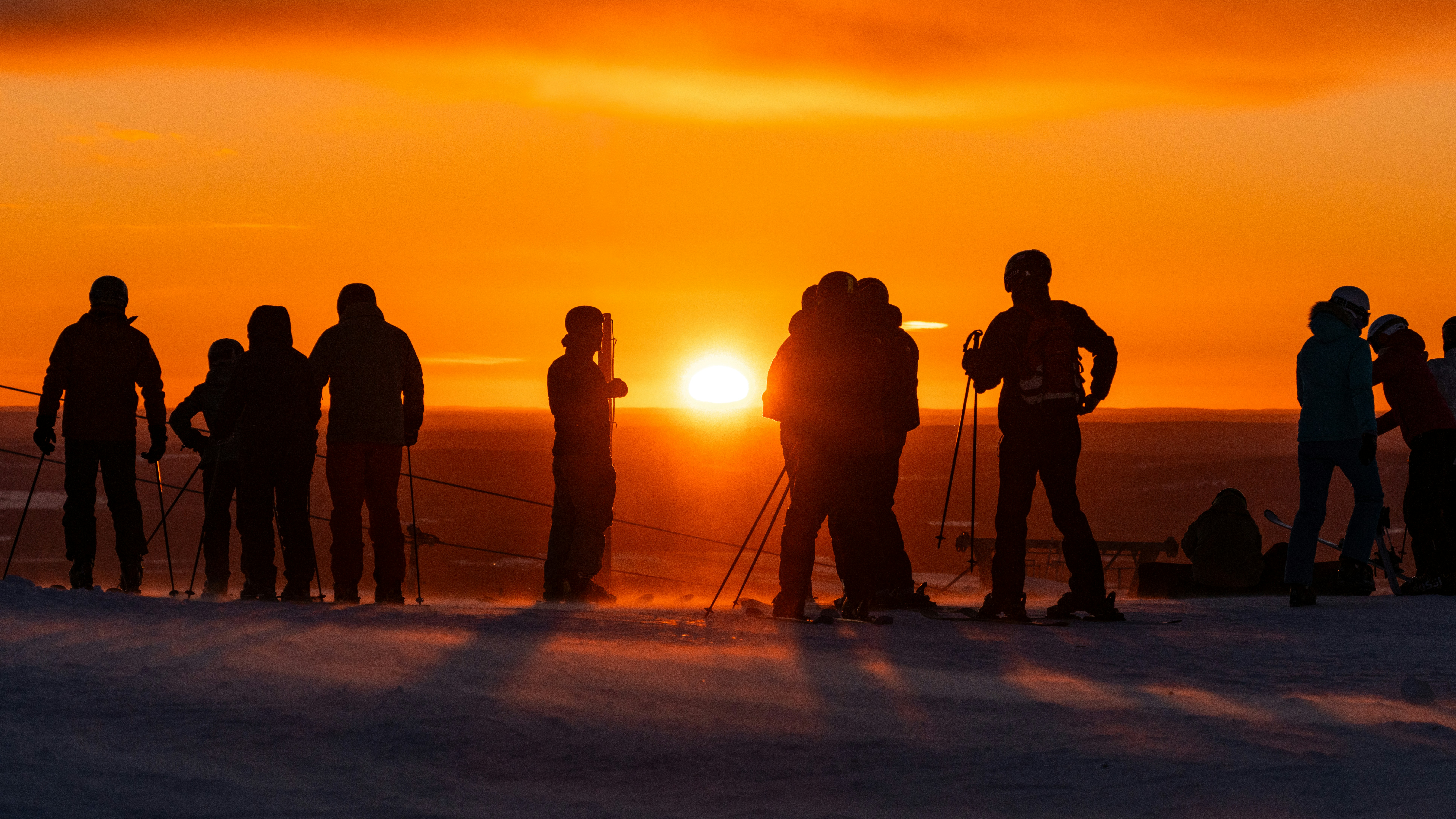 Silhouettes of people watching a vibrant sunset over snow