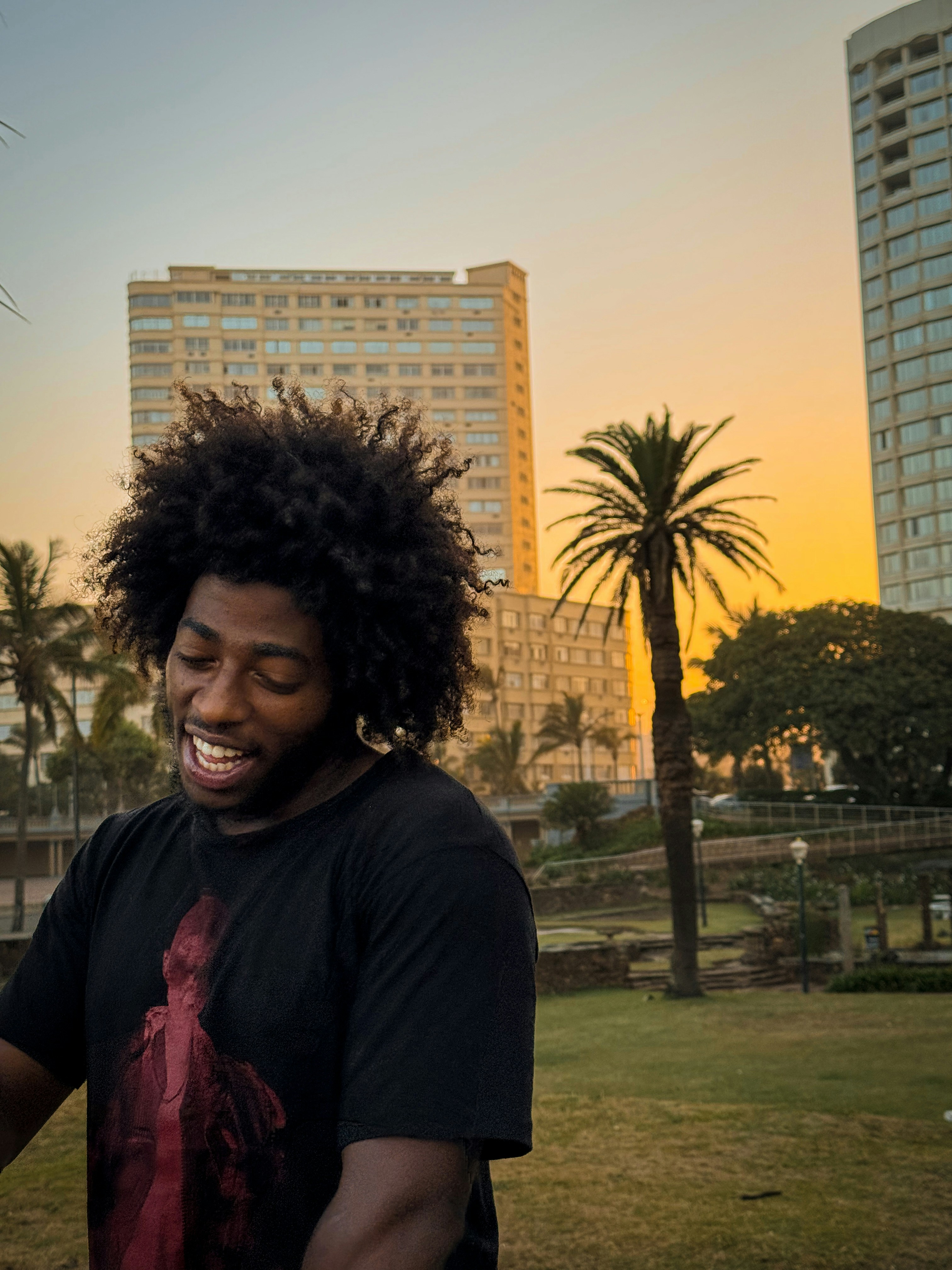 Homme à l’afro souriant avec des bâtiments et un palmier