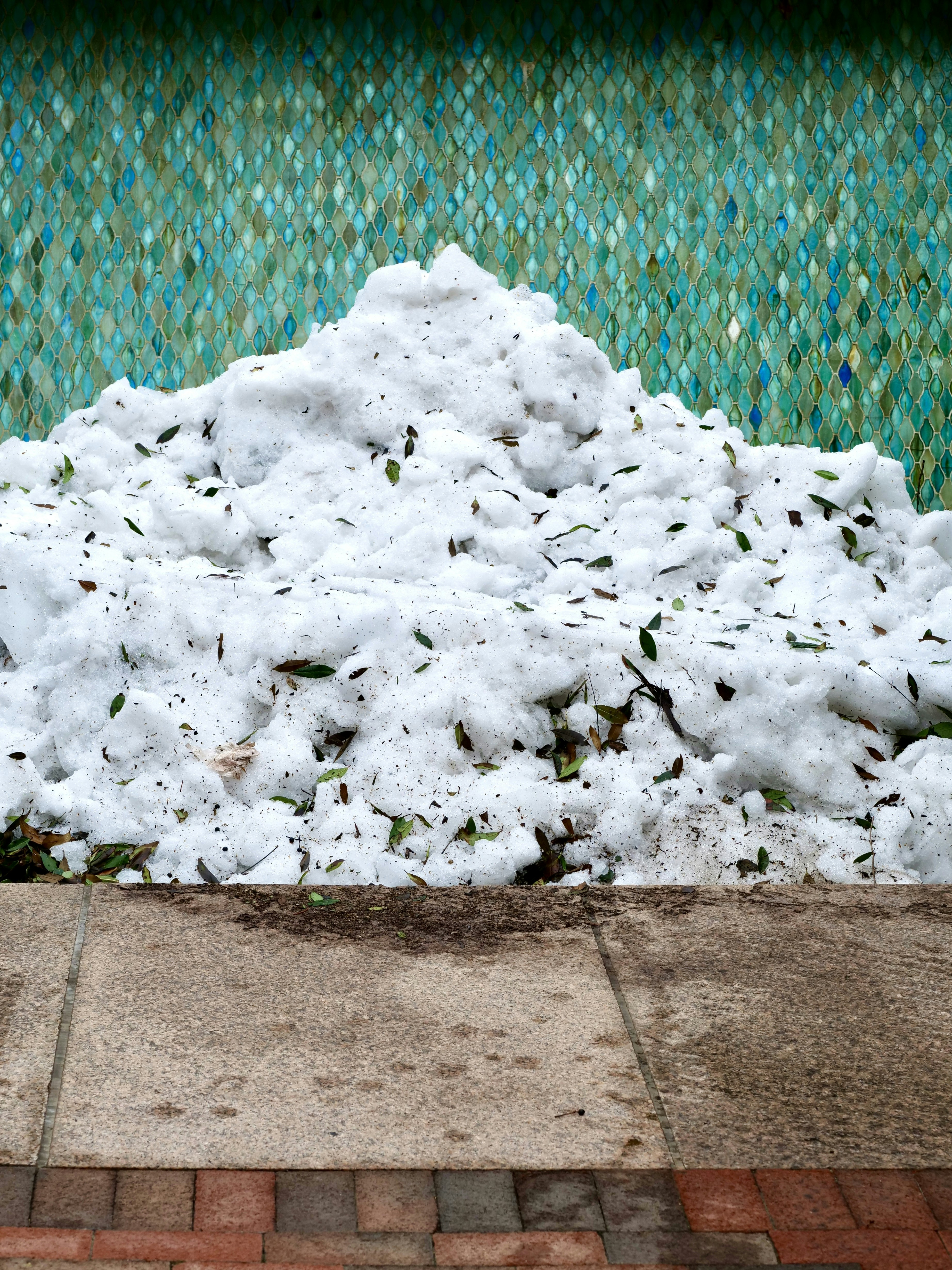 A large pile of snow sits against a tiled wall.