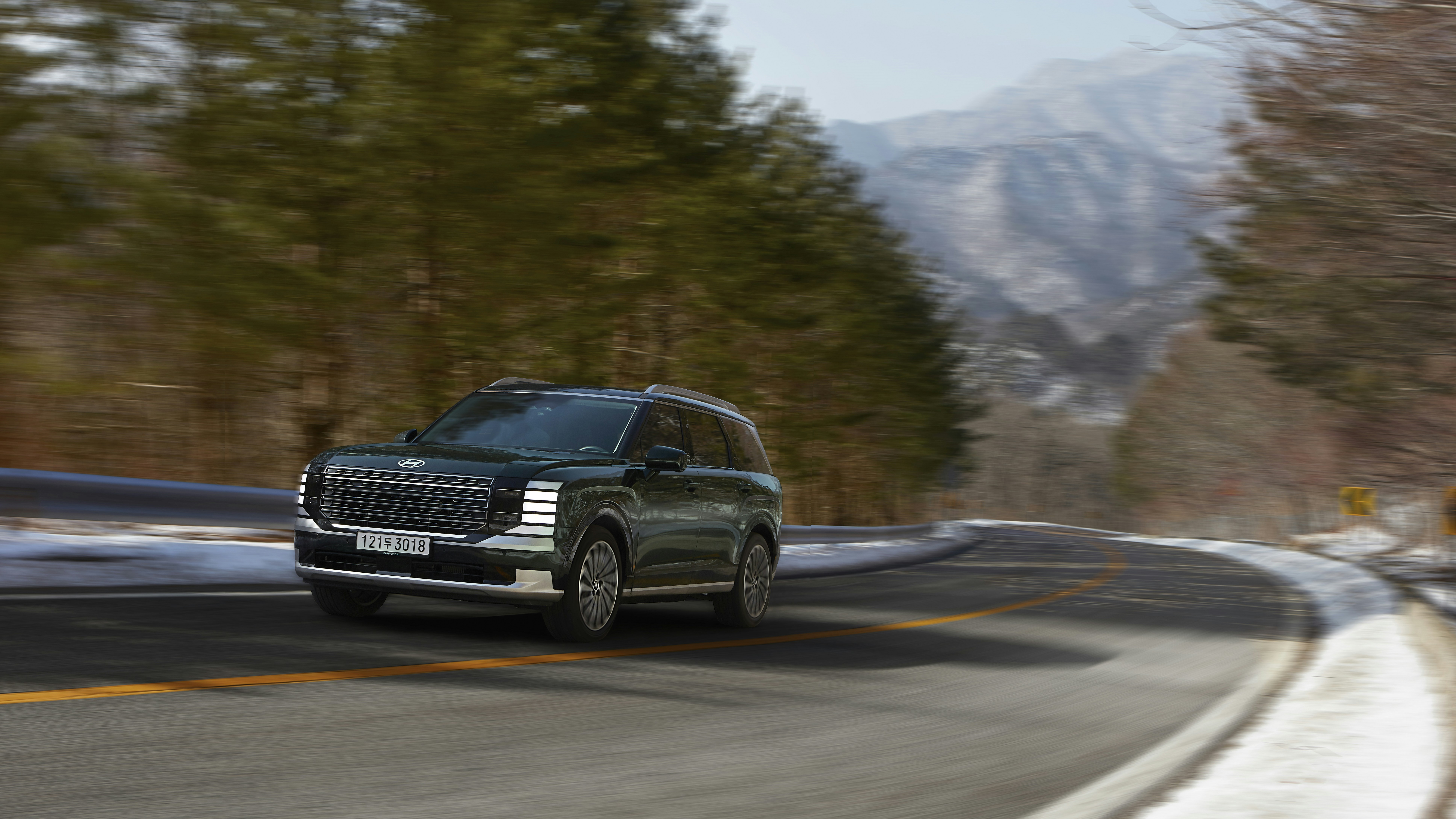 A dark suv drives on a winding road in winter.
