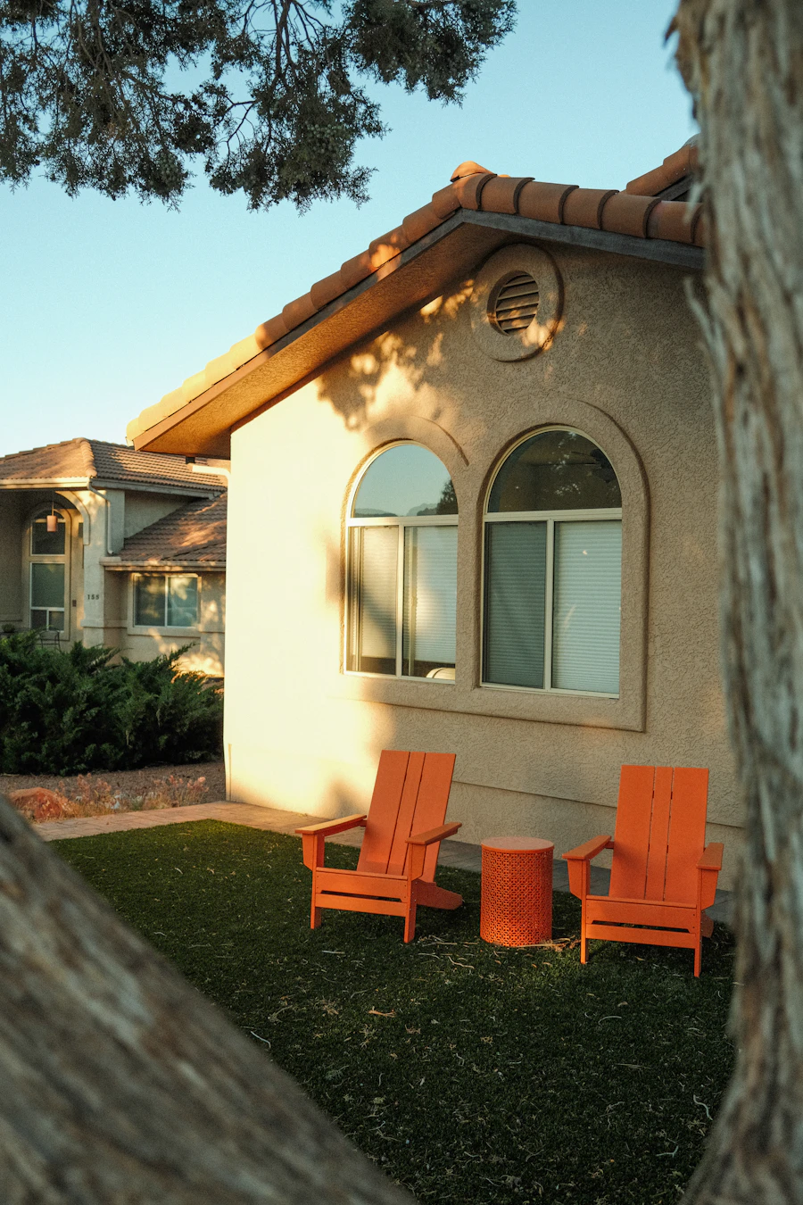 Stucco home with arched windows and two patio chairs in the evening sun