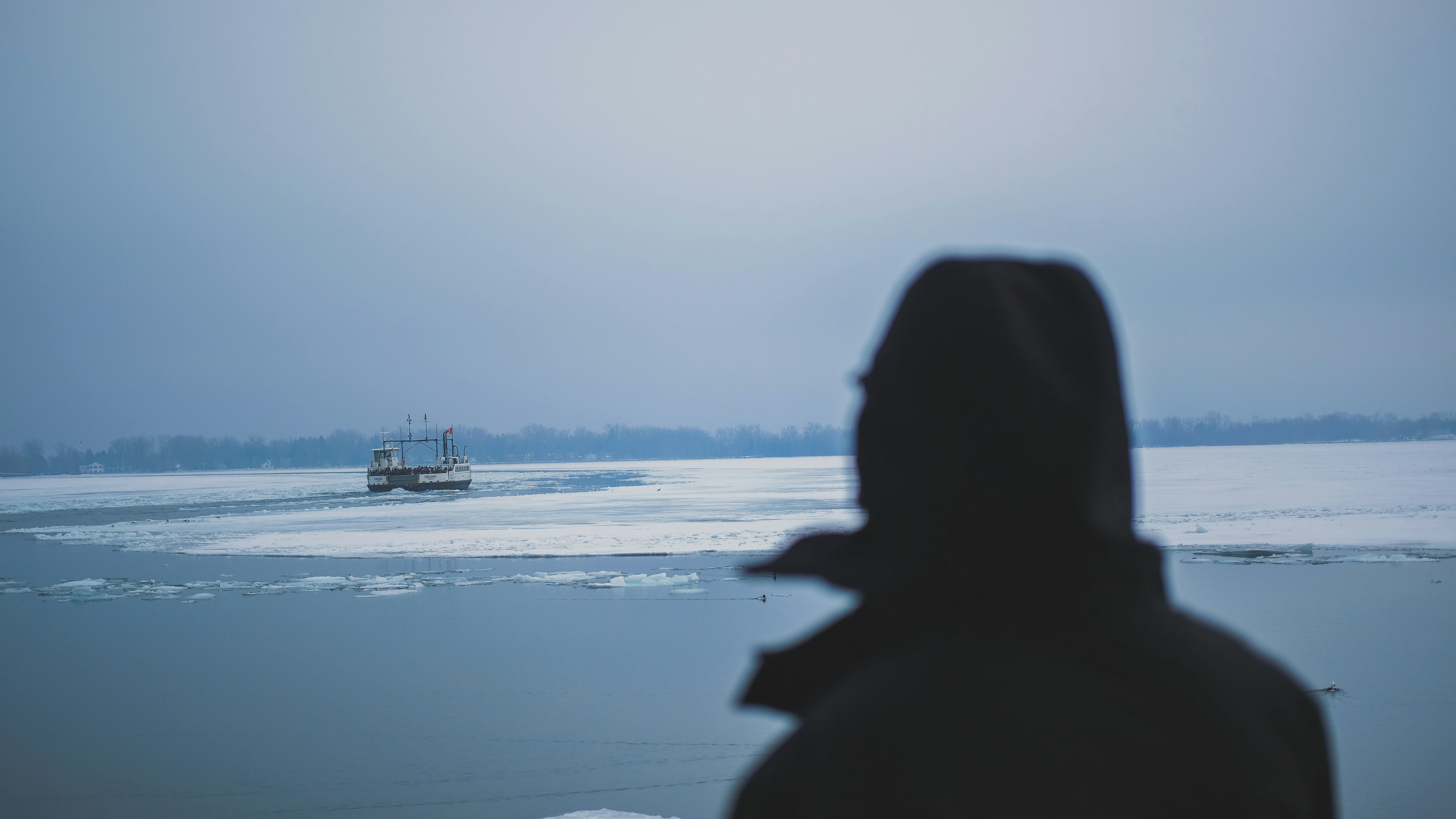 Person in hooded jacket looking at ice fishing shack.