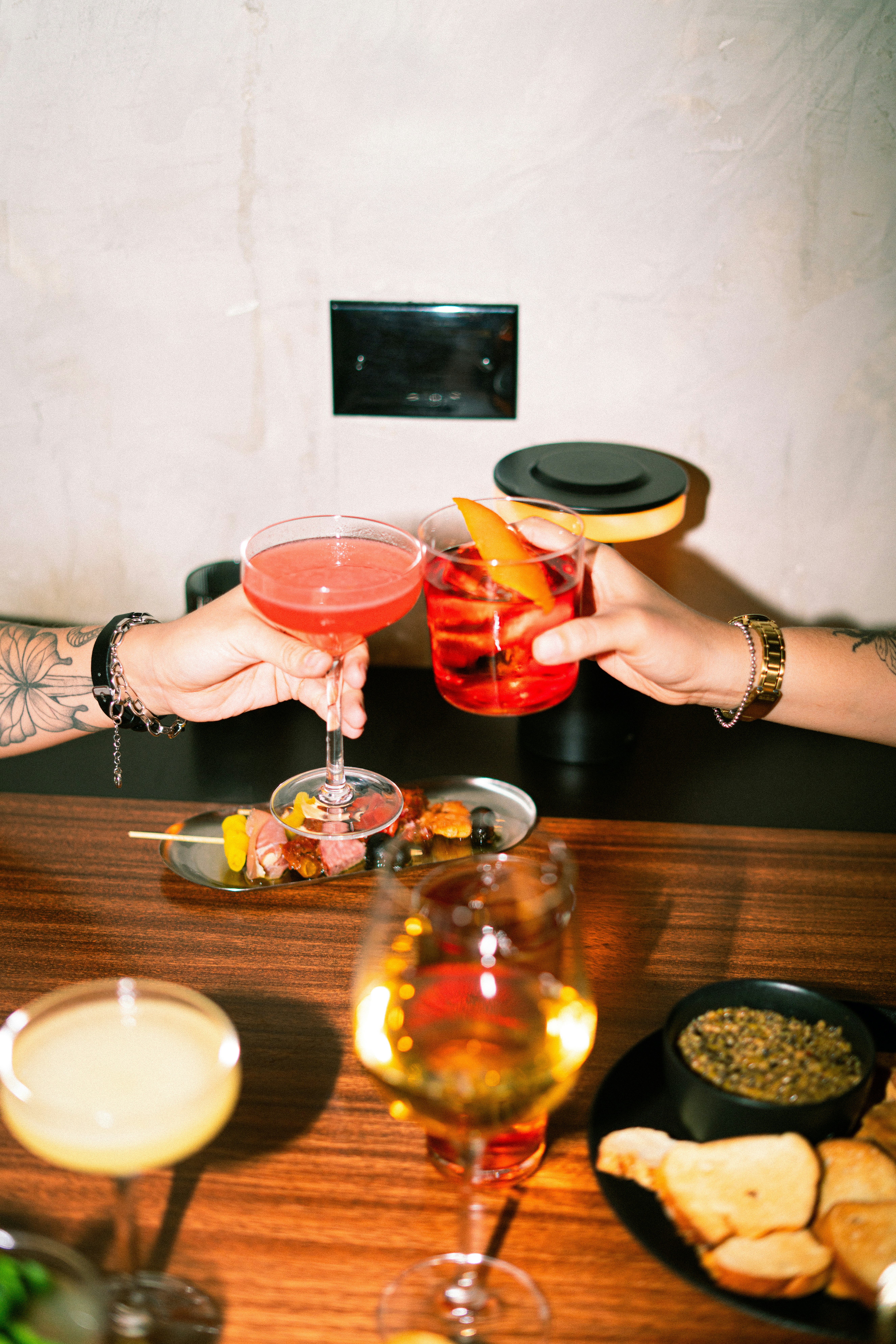 Two people clinking cocktail glasses over appetizers