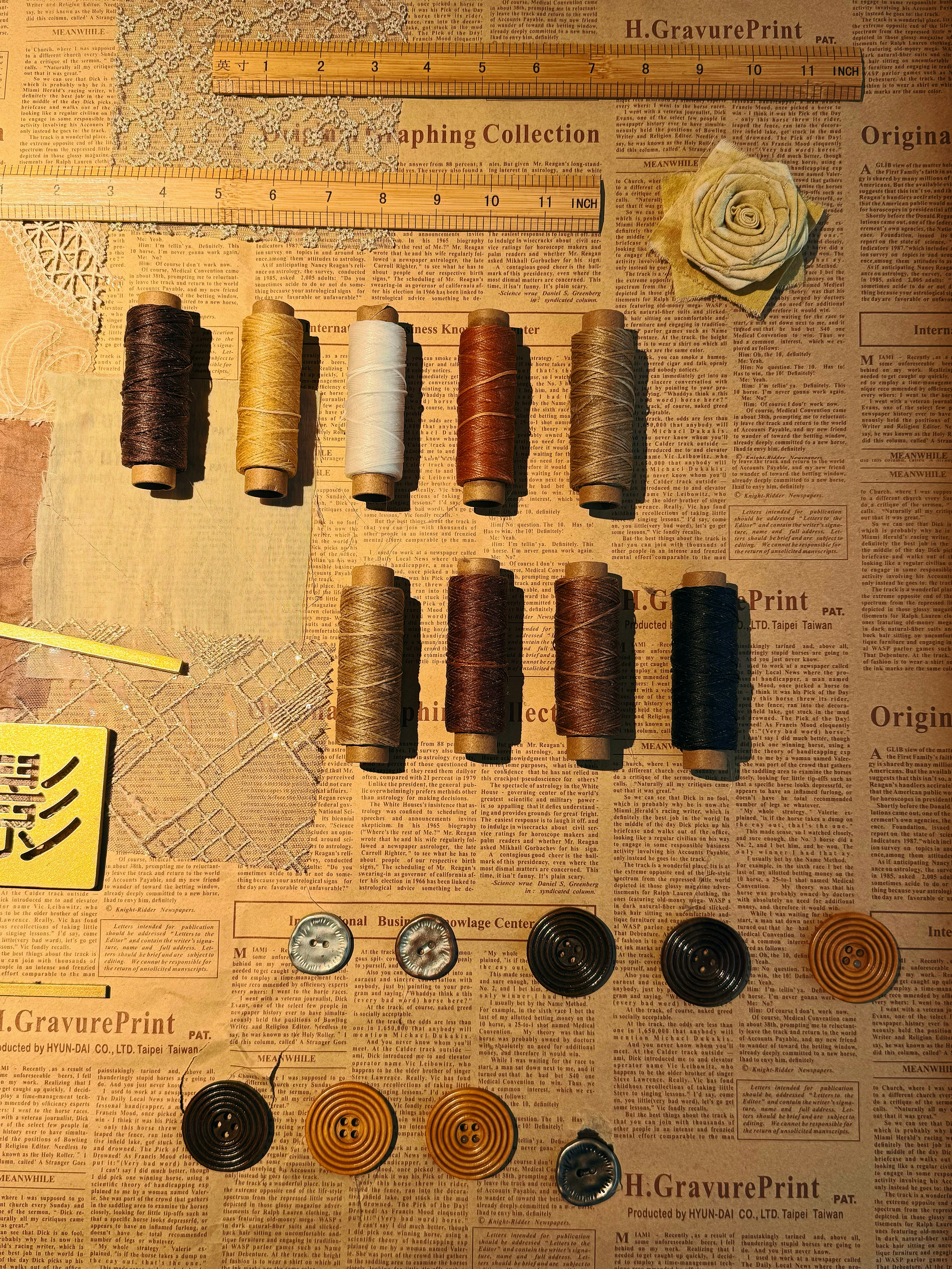 Various spools of thread, buttons, and rulers on newspaper.