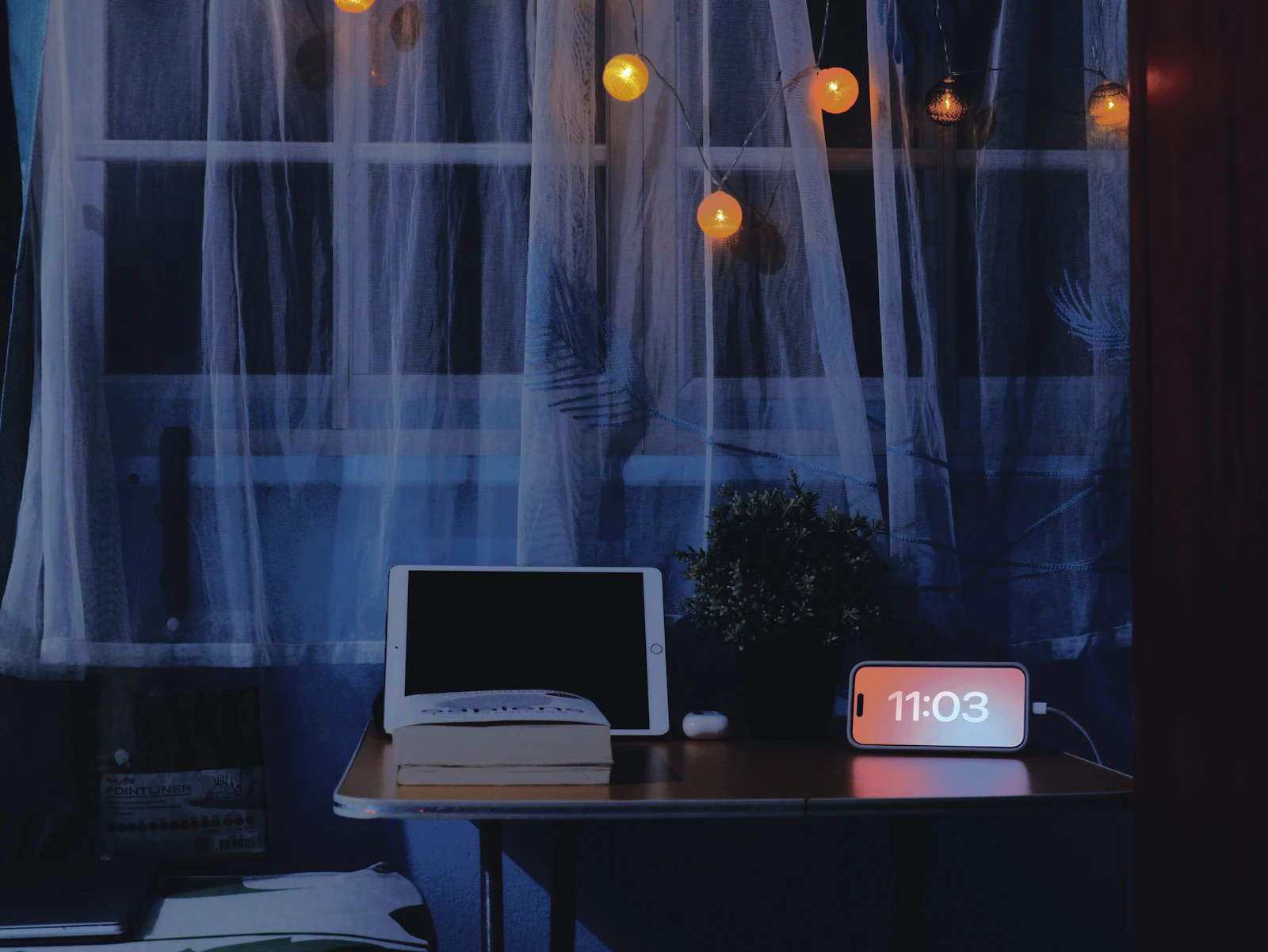 A desk lit late in the evening with a tablet, a book and a digital clock