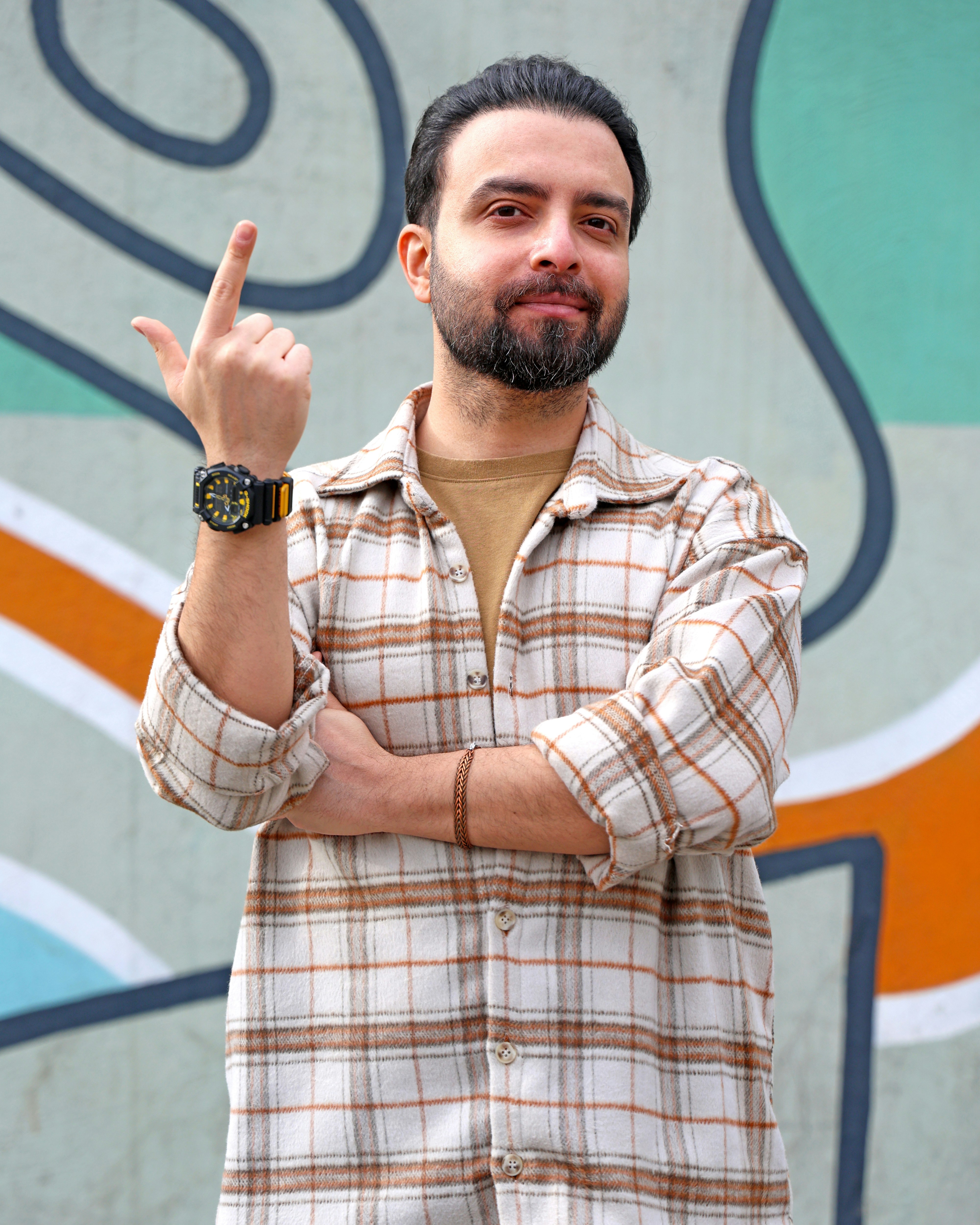 Uomo con la barba punta il dito davanti a un muro di graffiti.