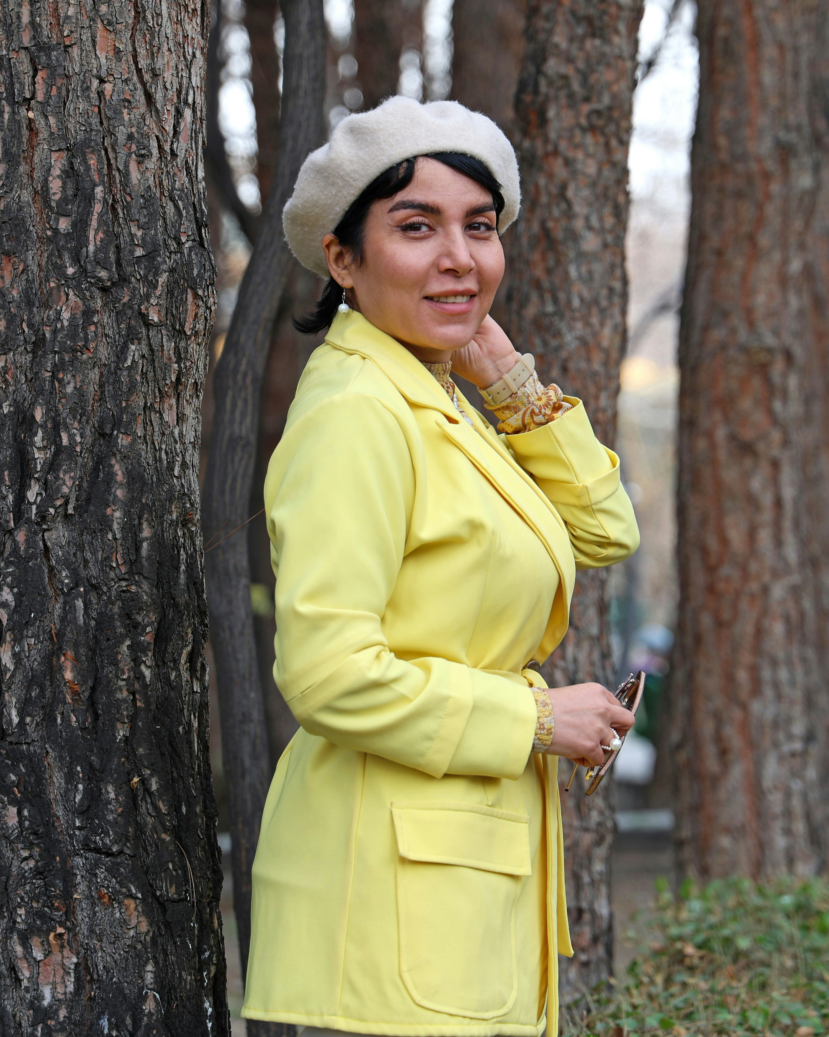 Donna con giacca gialla e basco posa all'aperto.