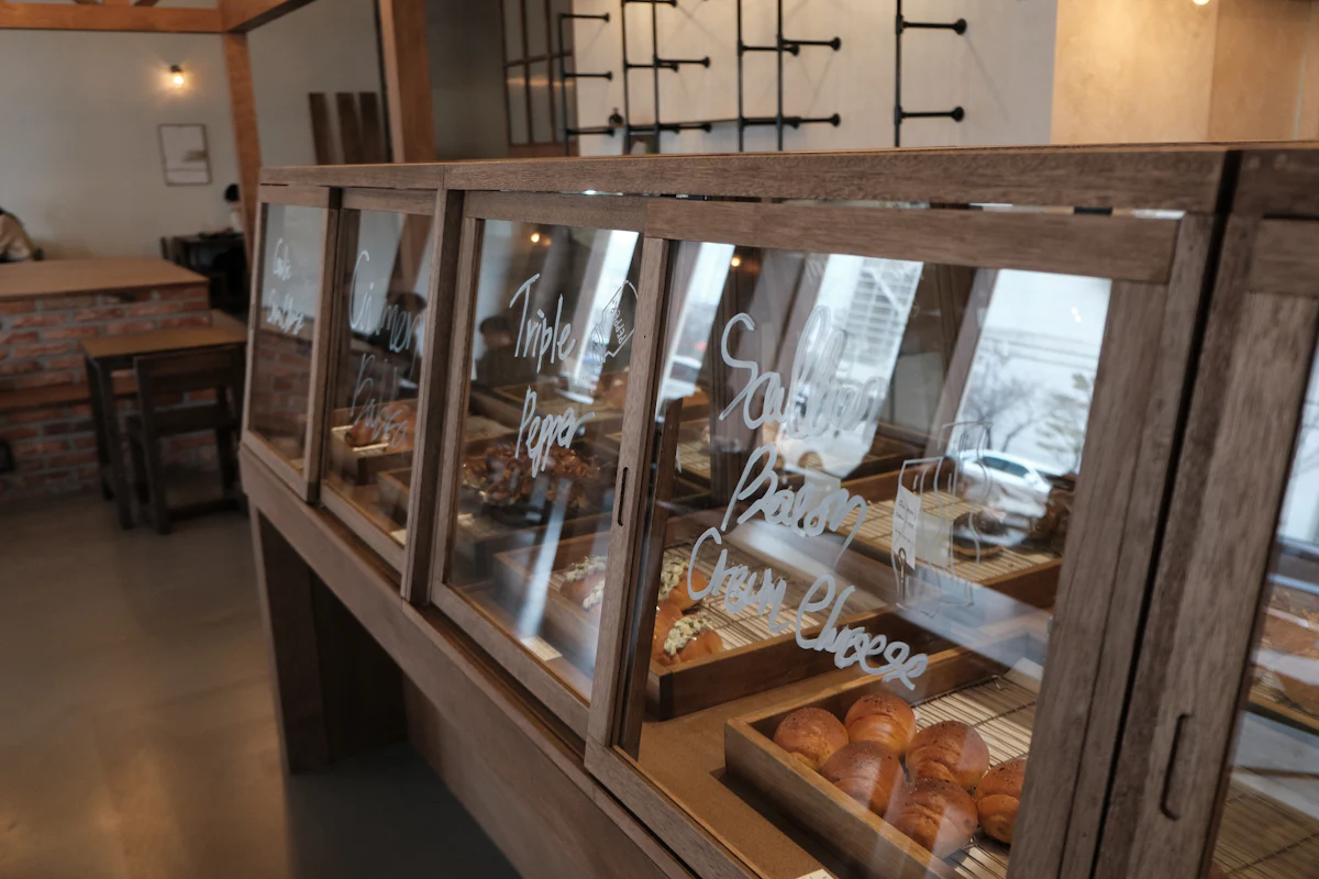 A wooden bakery display case lit warmly, filled with bread and rolls