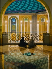Two people sit in a mosque with ornate decorations.