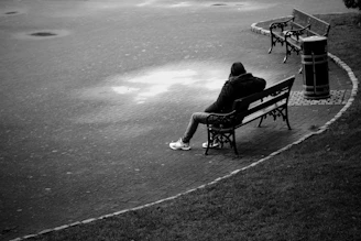 Person sits alone on a park bench in the rain.