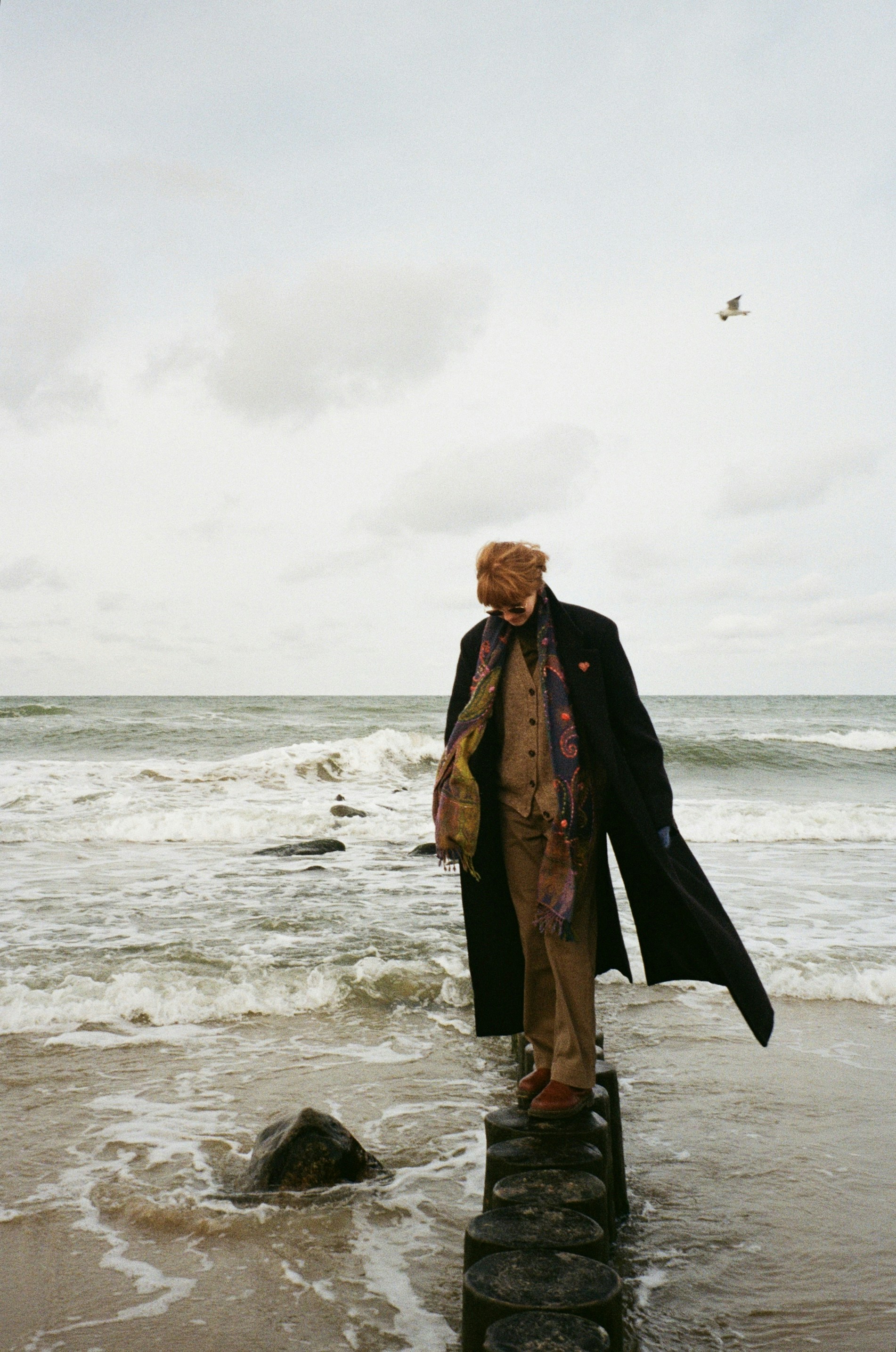 Man in coat stands on wooden posts by the sea