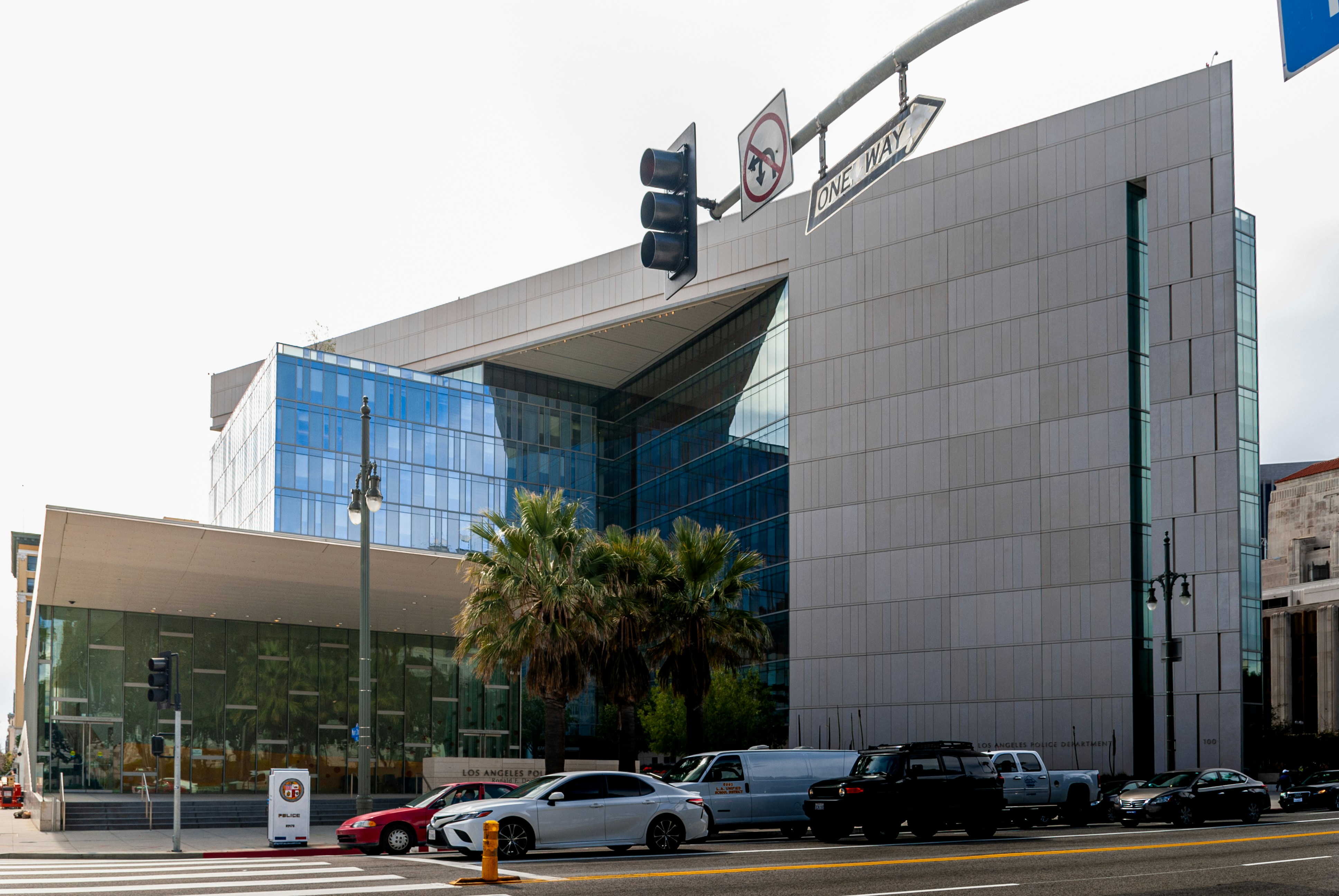 Modern glass building with palm trees and cars