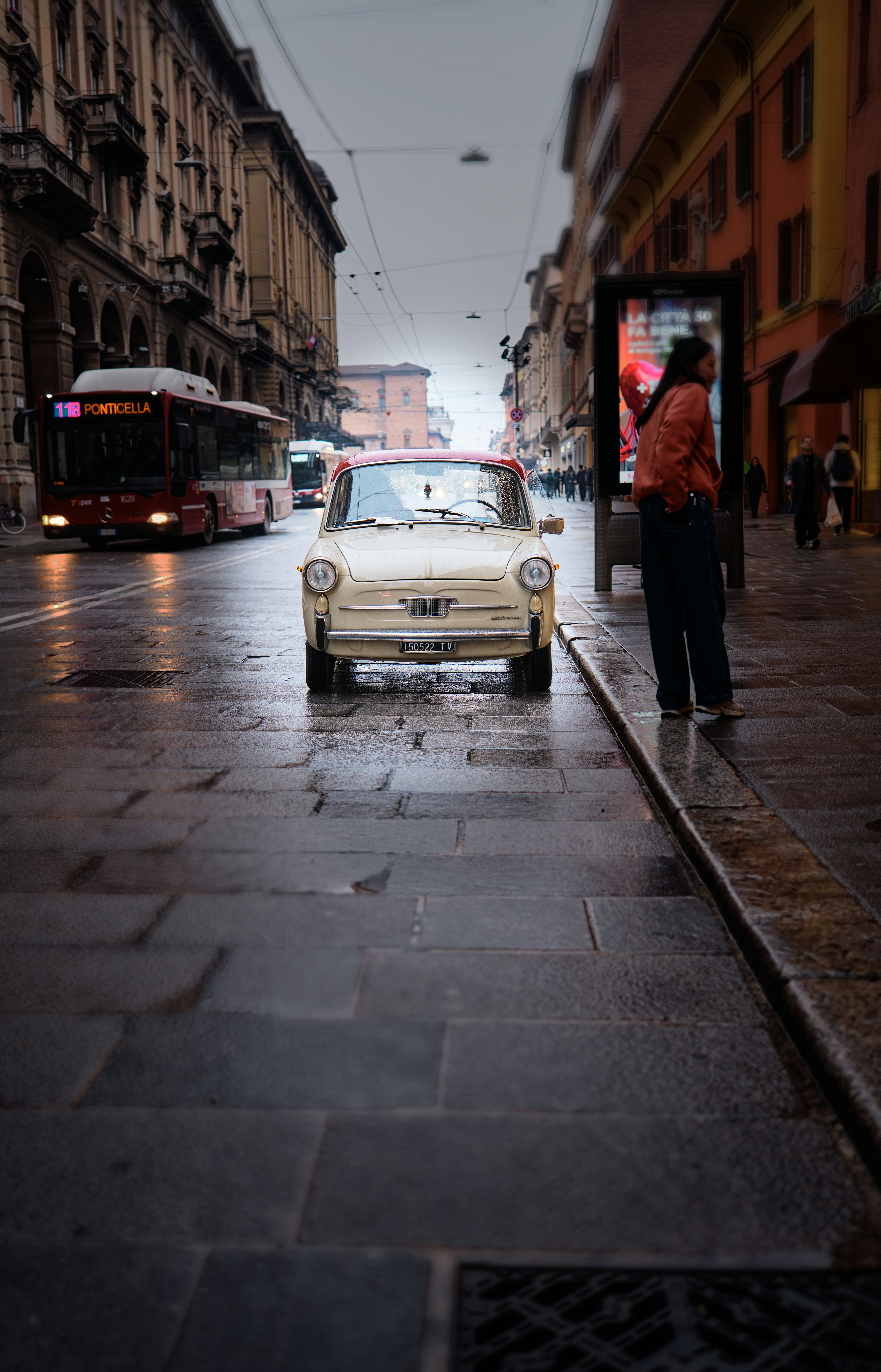 Vintage car parked on a wet city street with bus.