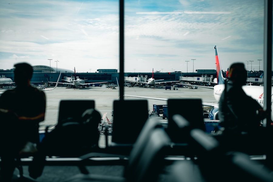 Silhouetted passengers wait at an airport gate window watching parked aircraft during a delay